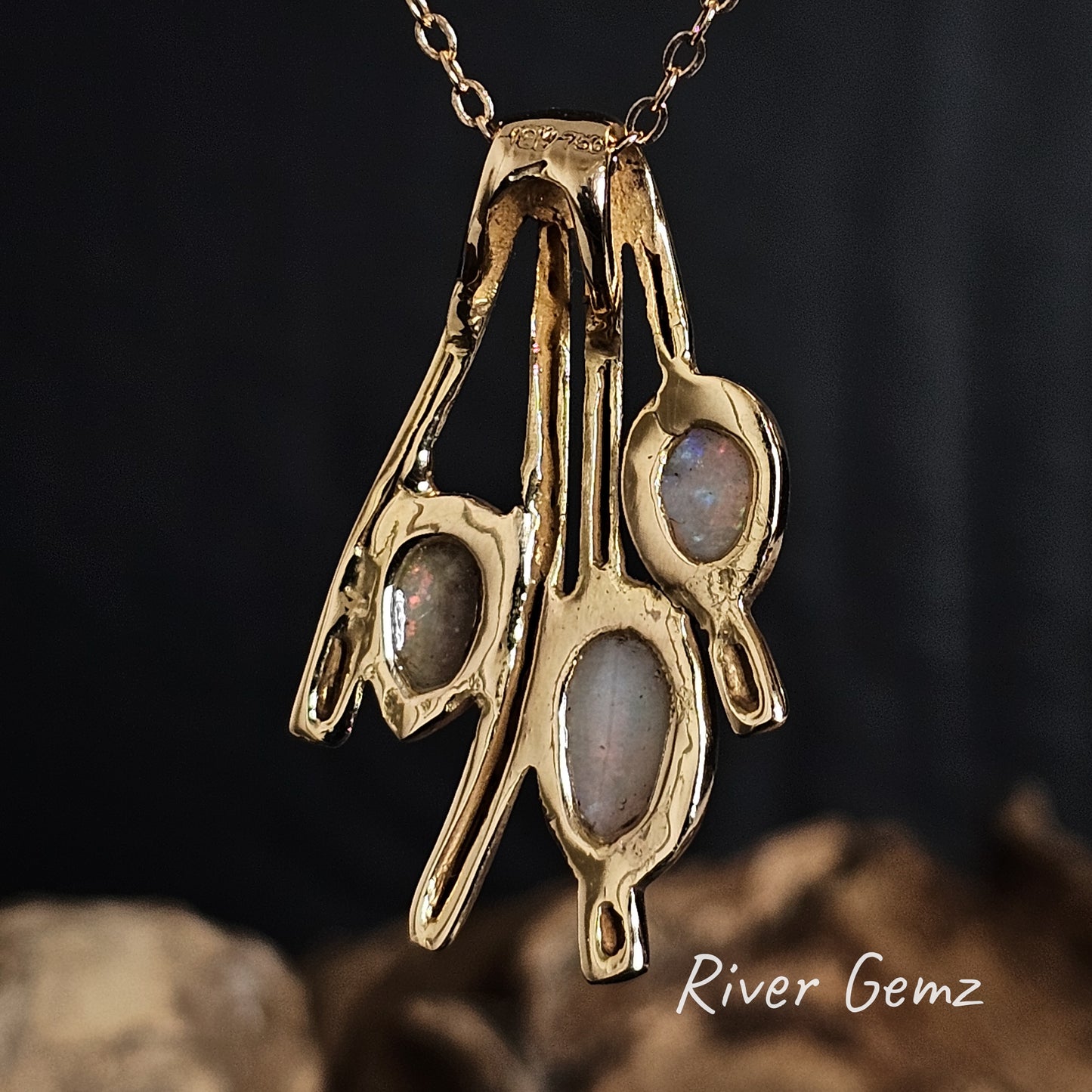 Back of gold pendant to show the light base tone of the three crystal opals on a dark background, featuring 'River Gemz' branding.