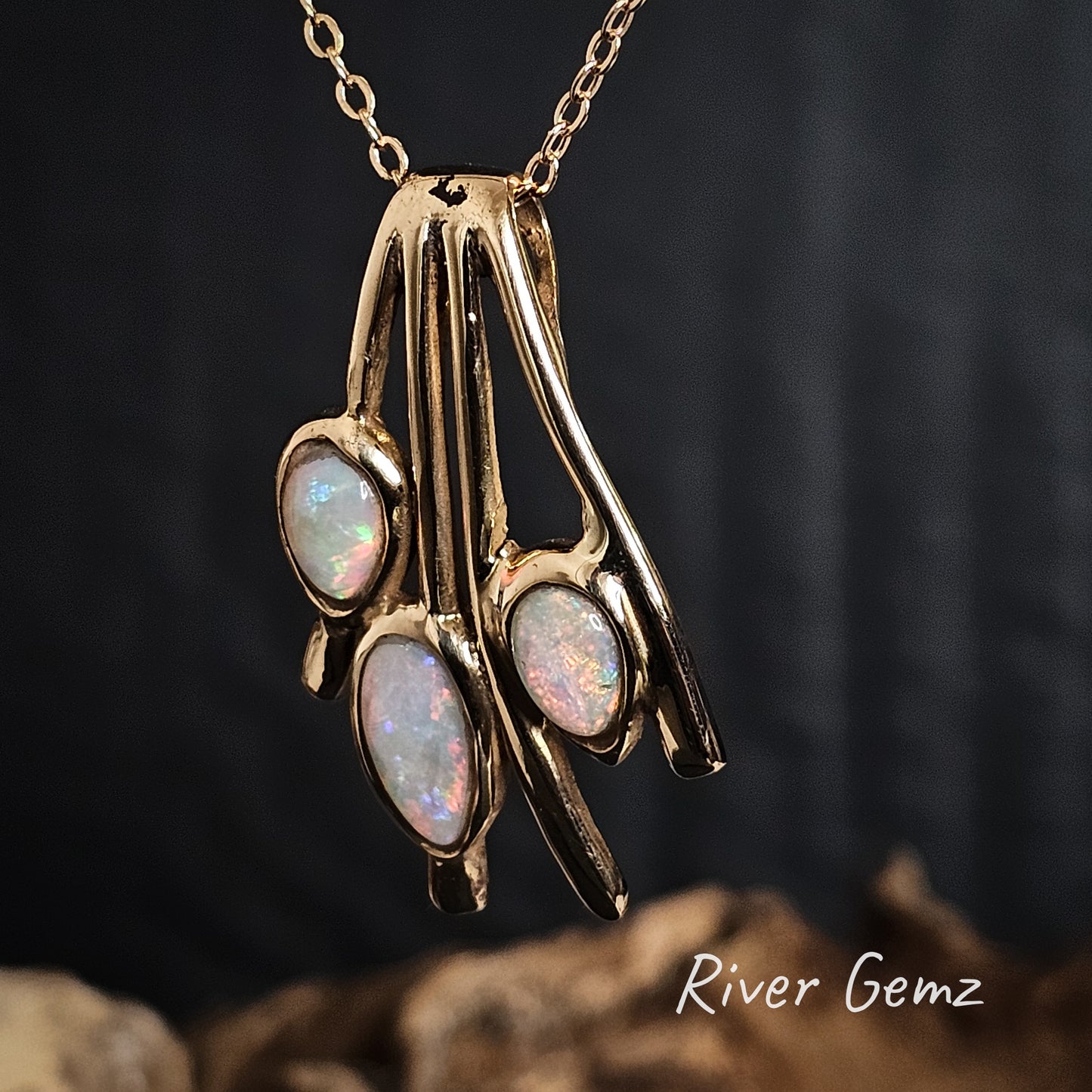 Gold pendant with three light opal stones on a dark background, featuring 'River Gemz' branding.