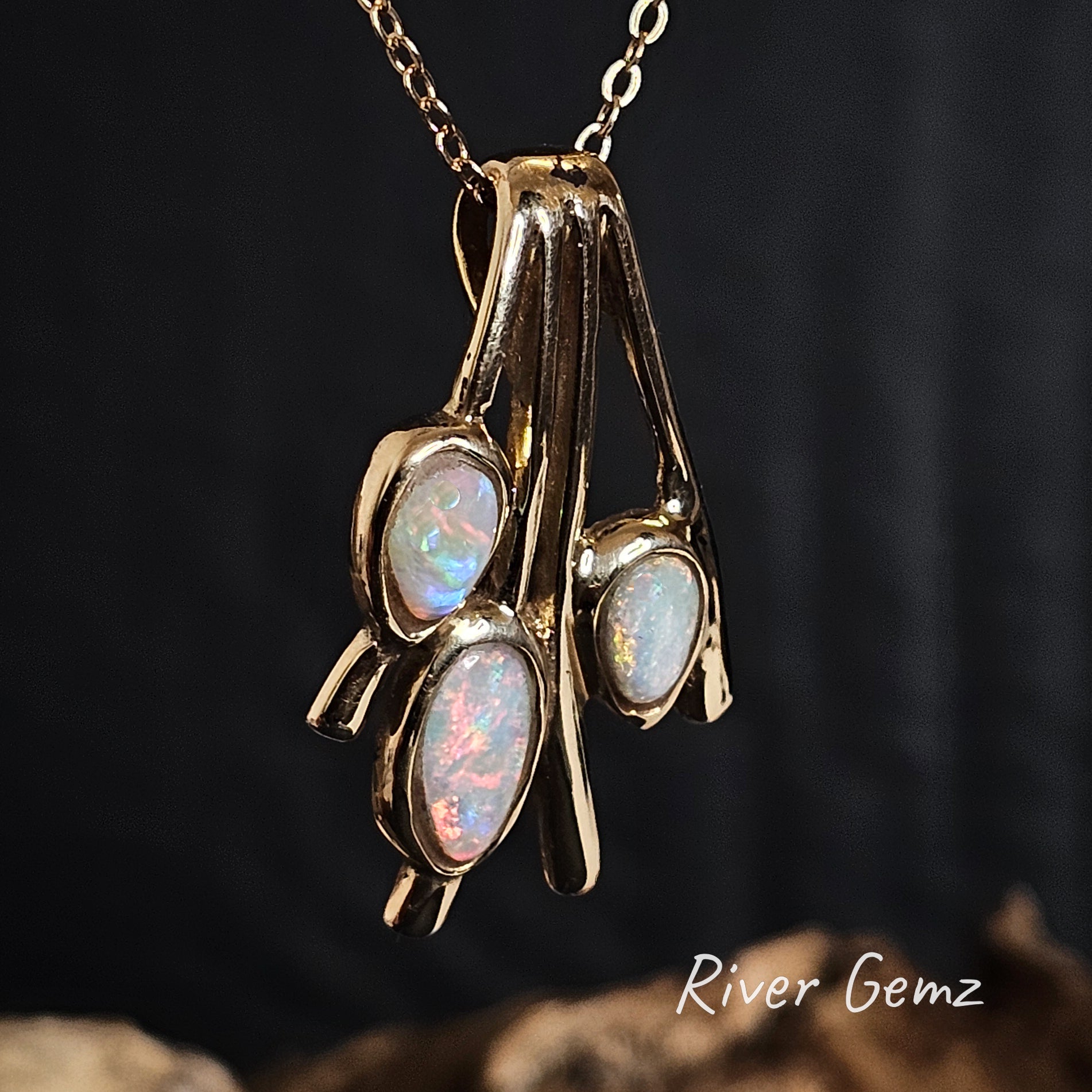 Gold pendant with 3 multi-coloured opal stones on a dark background, featuring the brand 'River Gemz'.