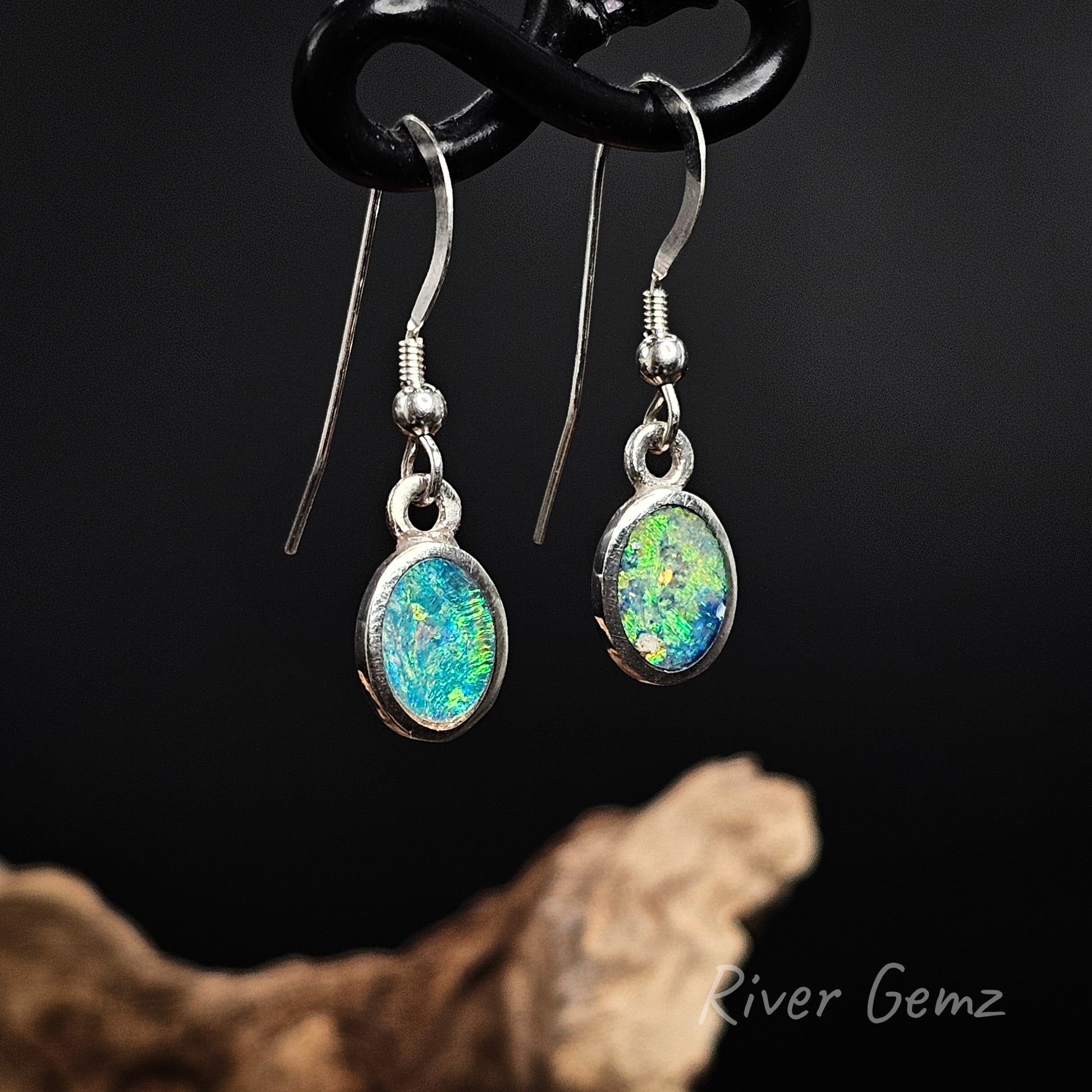 Opal earrings hanging on a black background with 'River Gemz' branding.
