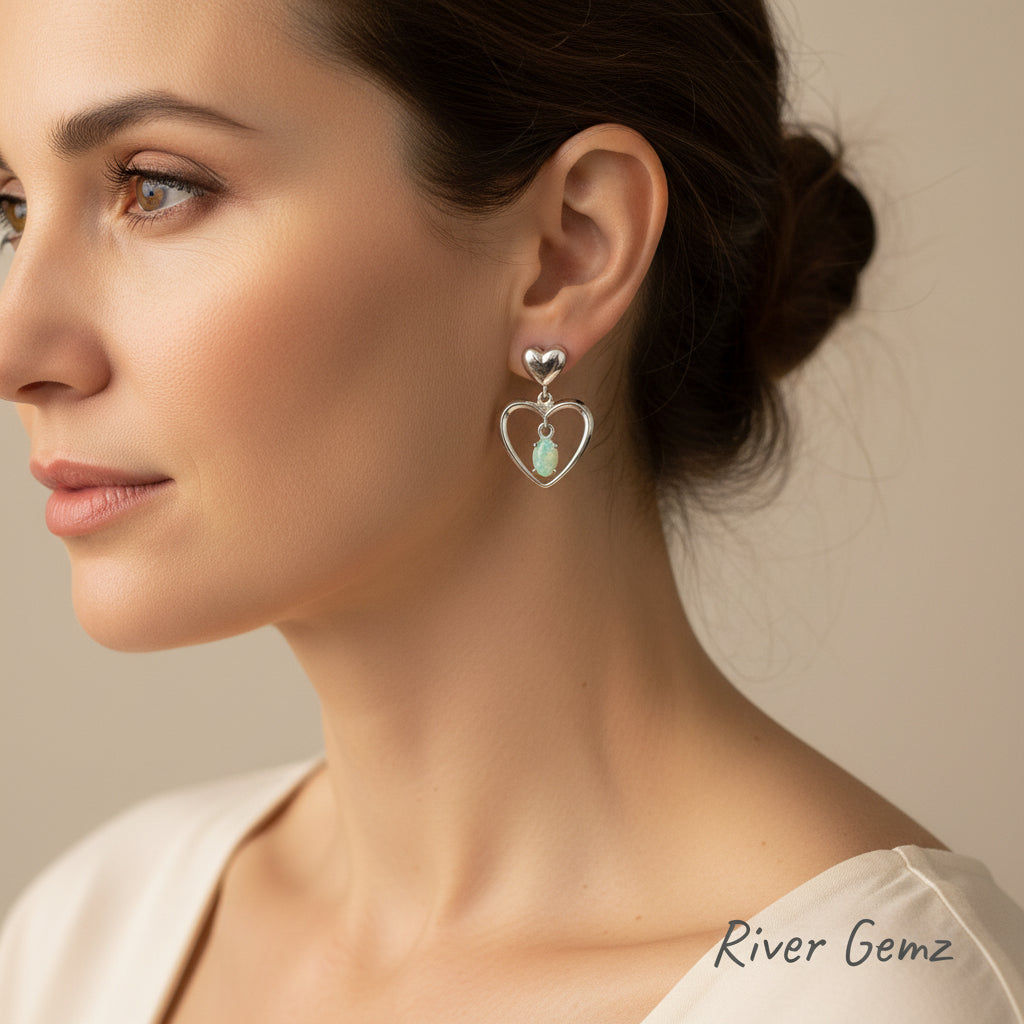 Heart-shaped silver earrings with opal stones on a dark background, branded 'River Gemz'.