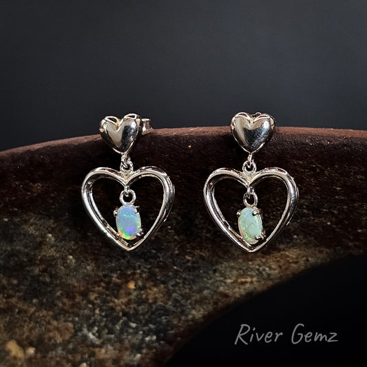 Heart-shaped earrings with opal stones on a dark background, branded 'River Gemz'.
