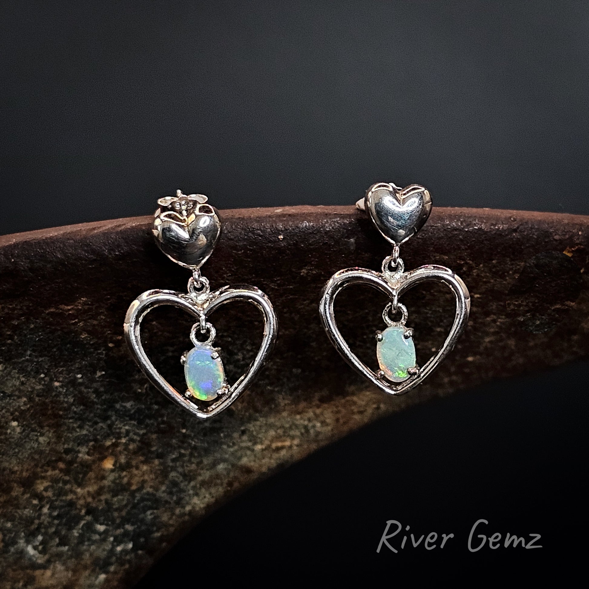 Heart-shaped earrings with opal stones on a dark background, branded 'River Gemz'.