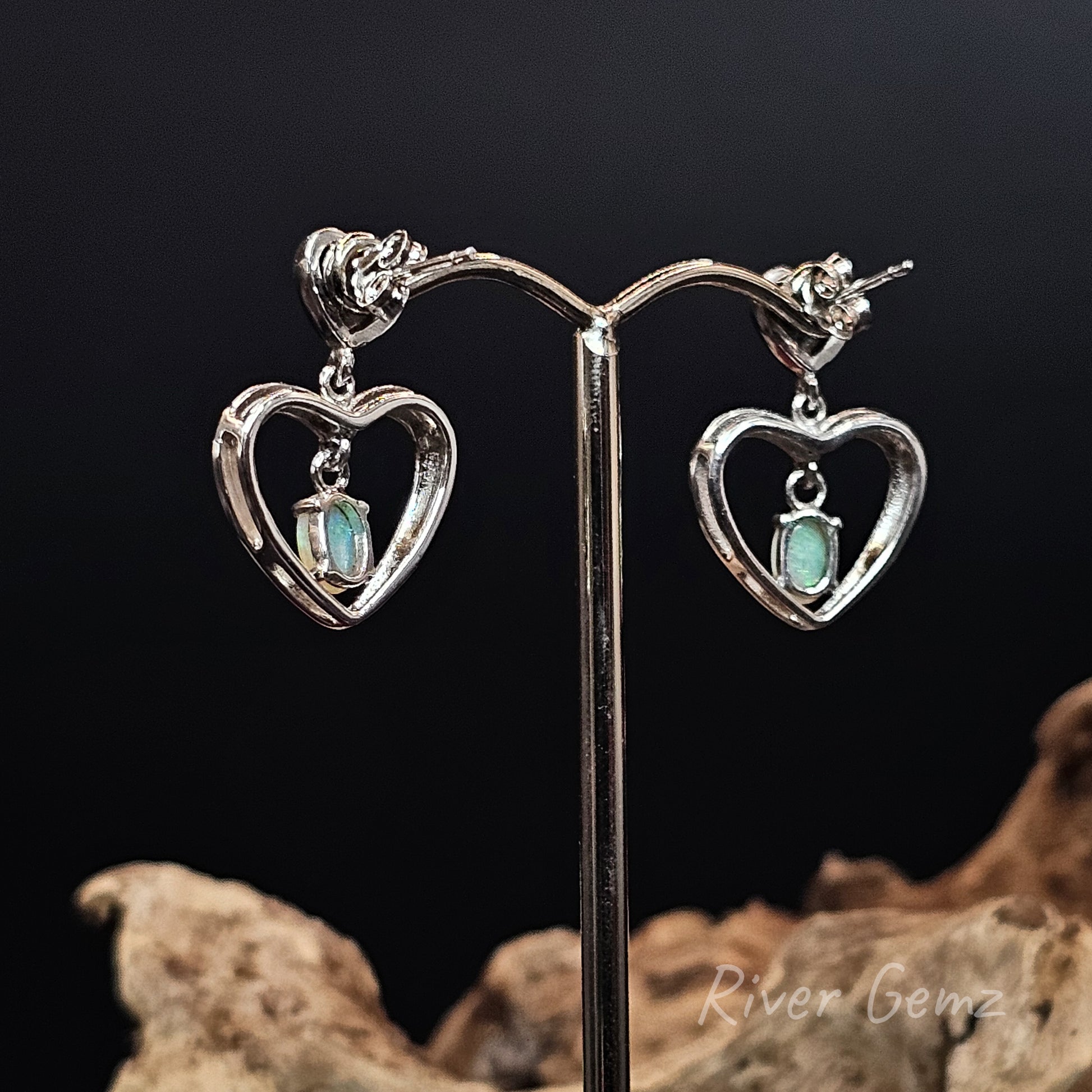Back view of heart-shaped earrings showing the light base tone of the crystal opals on a stand against a dark background