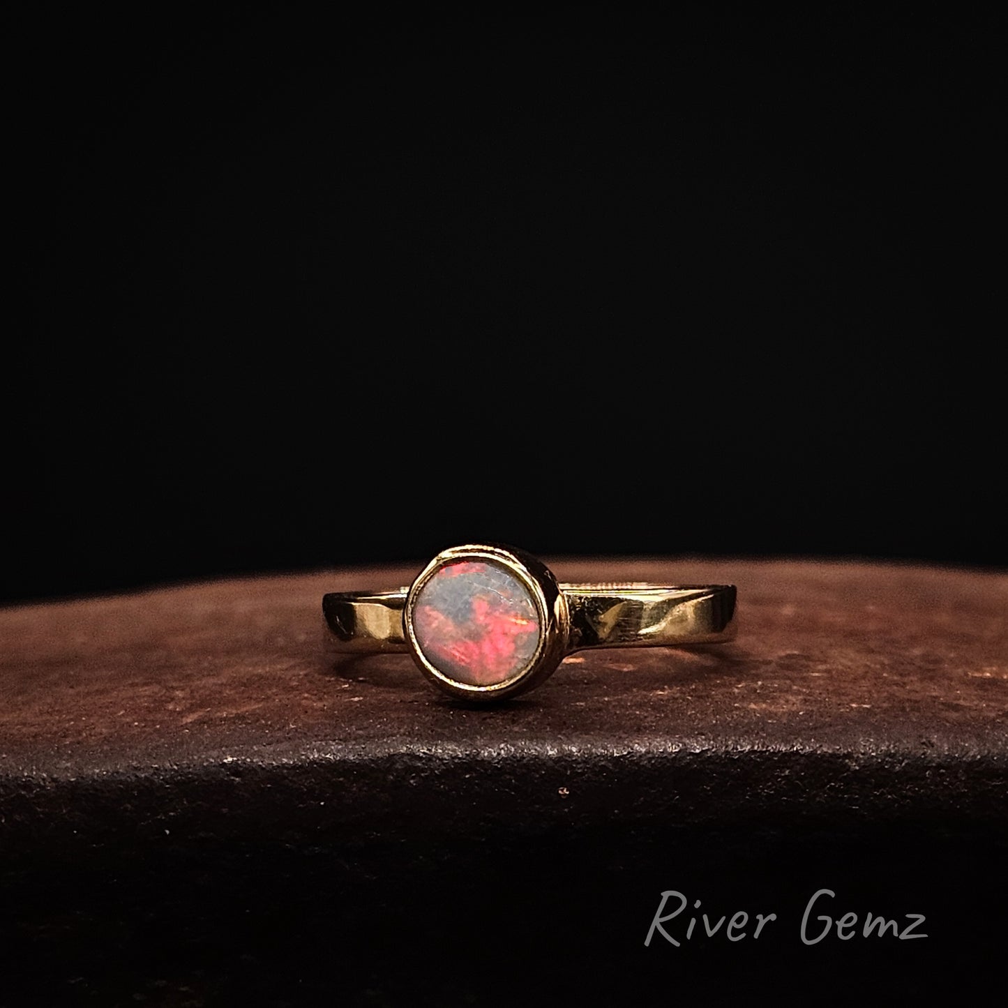 Round opal with strong red colouration besel set in yellow gold ring.
