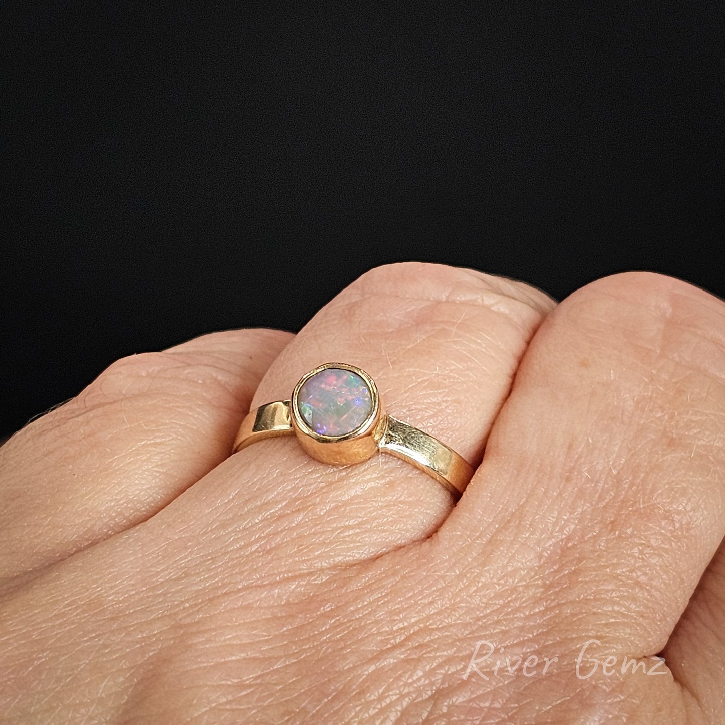Gold ring with an opal stone on a hand against a black background