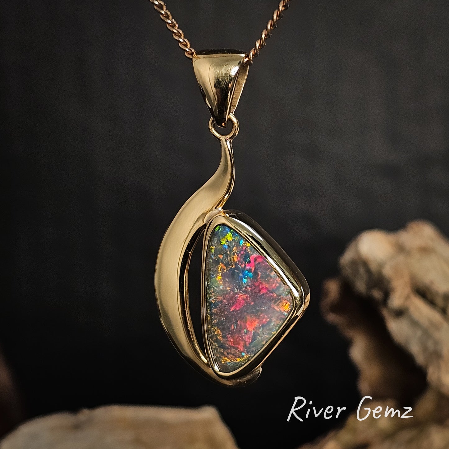 Gold necklace with a colorful dark opal on a dark background, featuring 'River Gemz' branding.