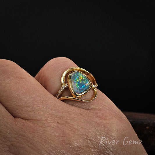 Multi-coloured dark opal set in yellow gold ring with diamonds shown worn on right hand pinky finger. Black background and 'River Gemz' watermark in the bottom right hand corner.
