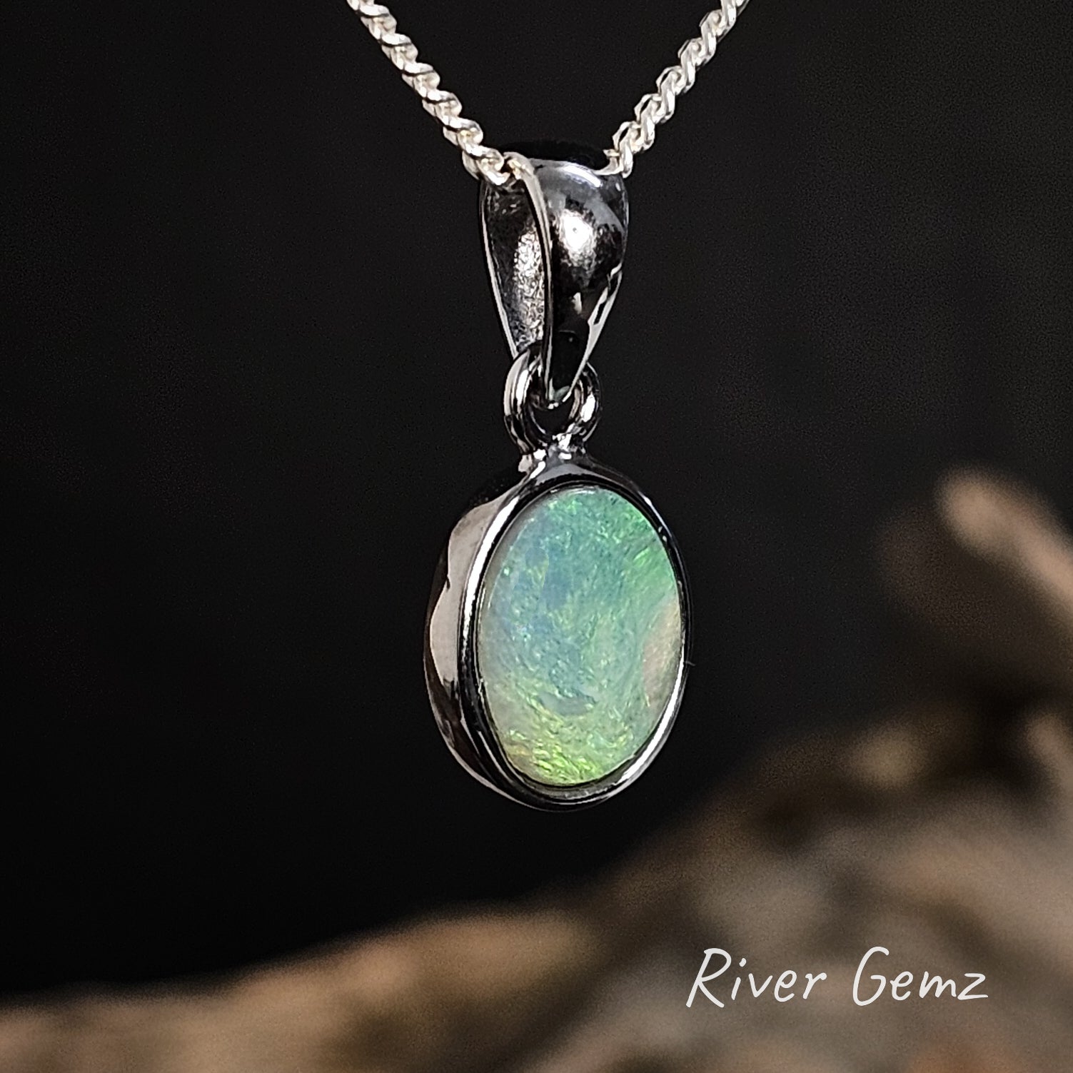 Semi-black opal pendant with a large bail a dark background with 'River Gemz' branding.
