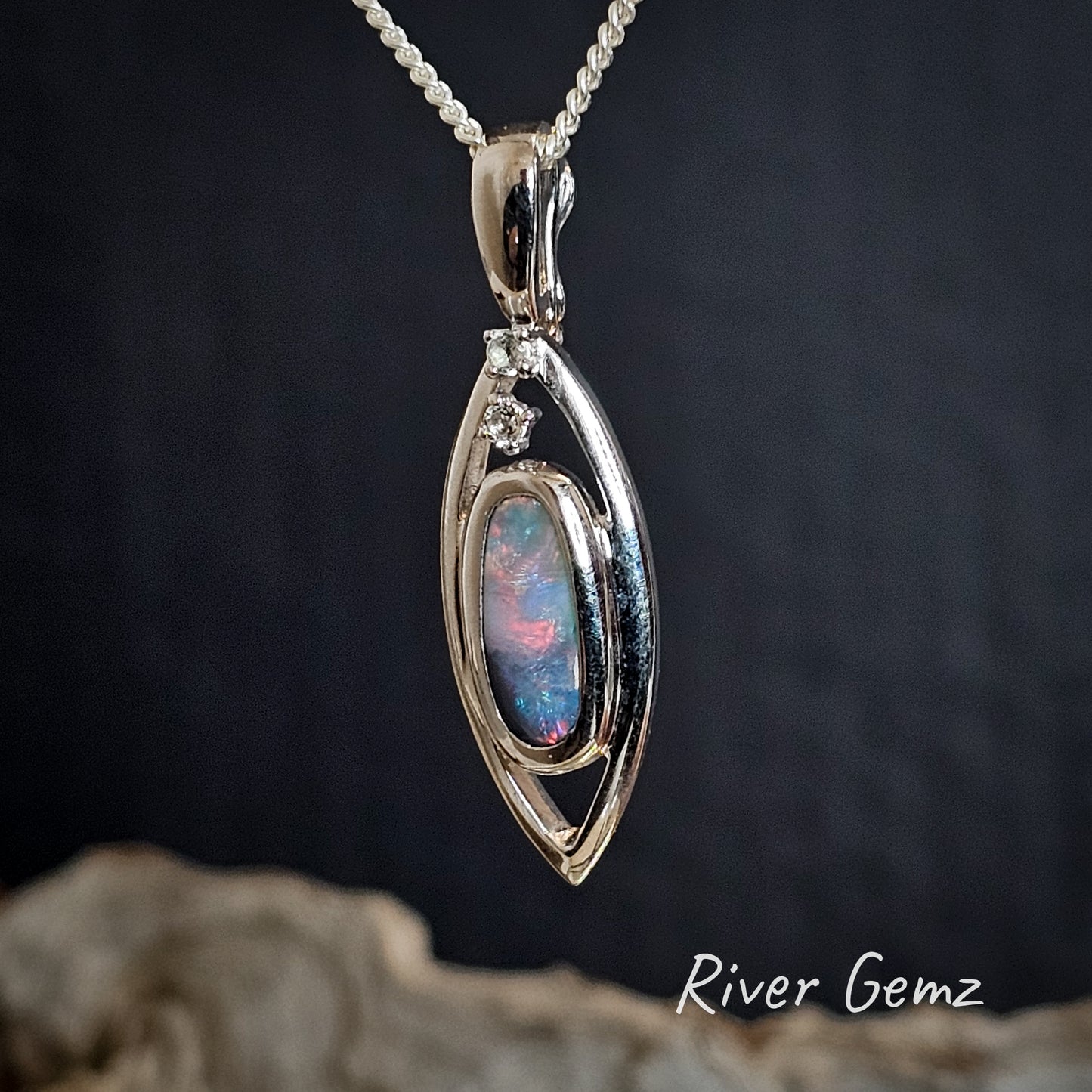 Oval shaped multi-coloured dark opal and white topaz in a silver pendant.