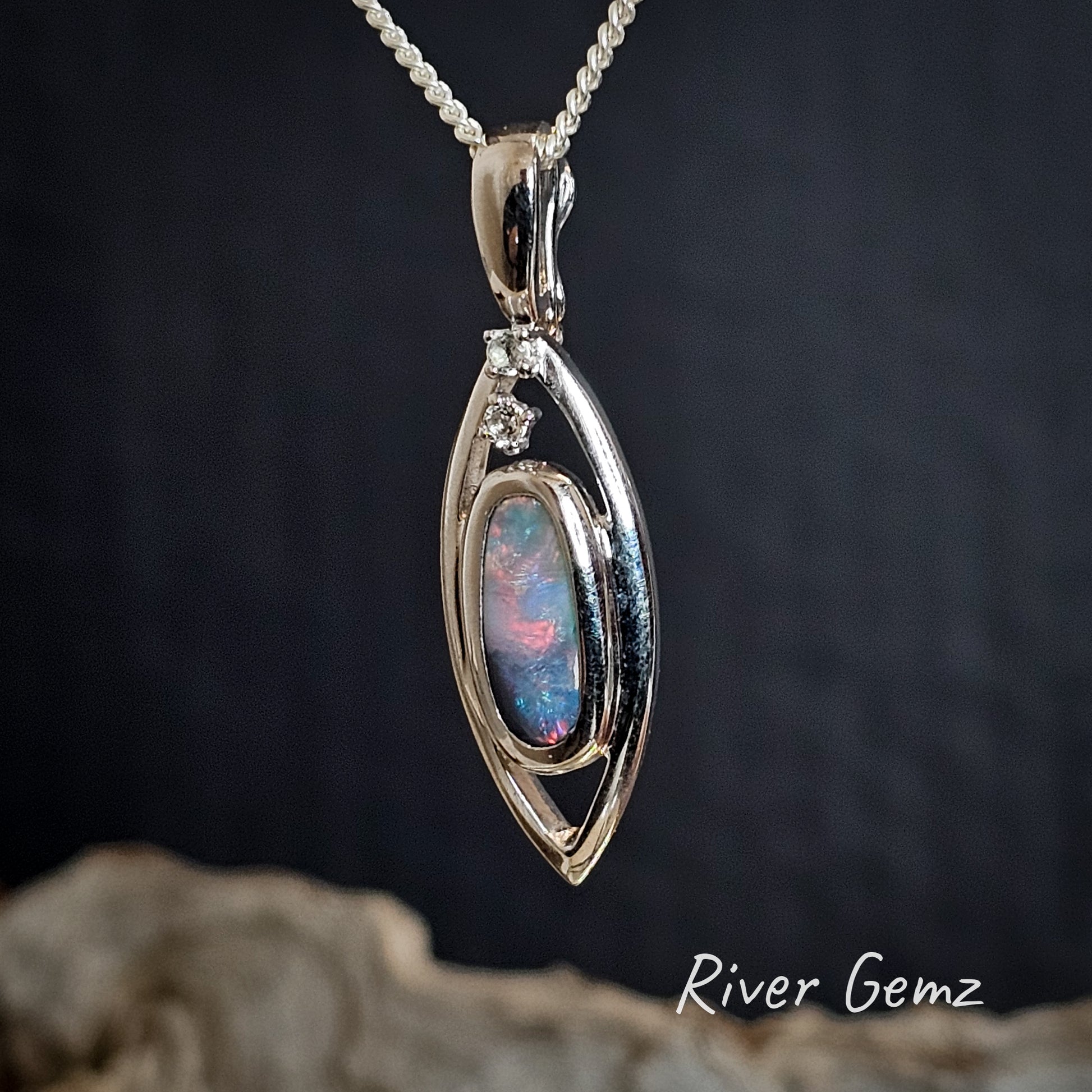Oval shaped multi-coloured dark opal and white topaz in a silver pendant.
