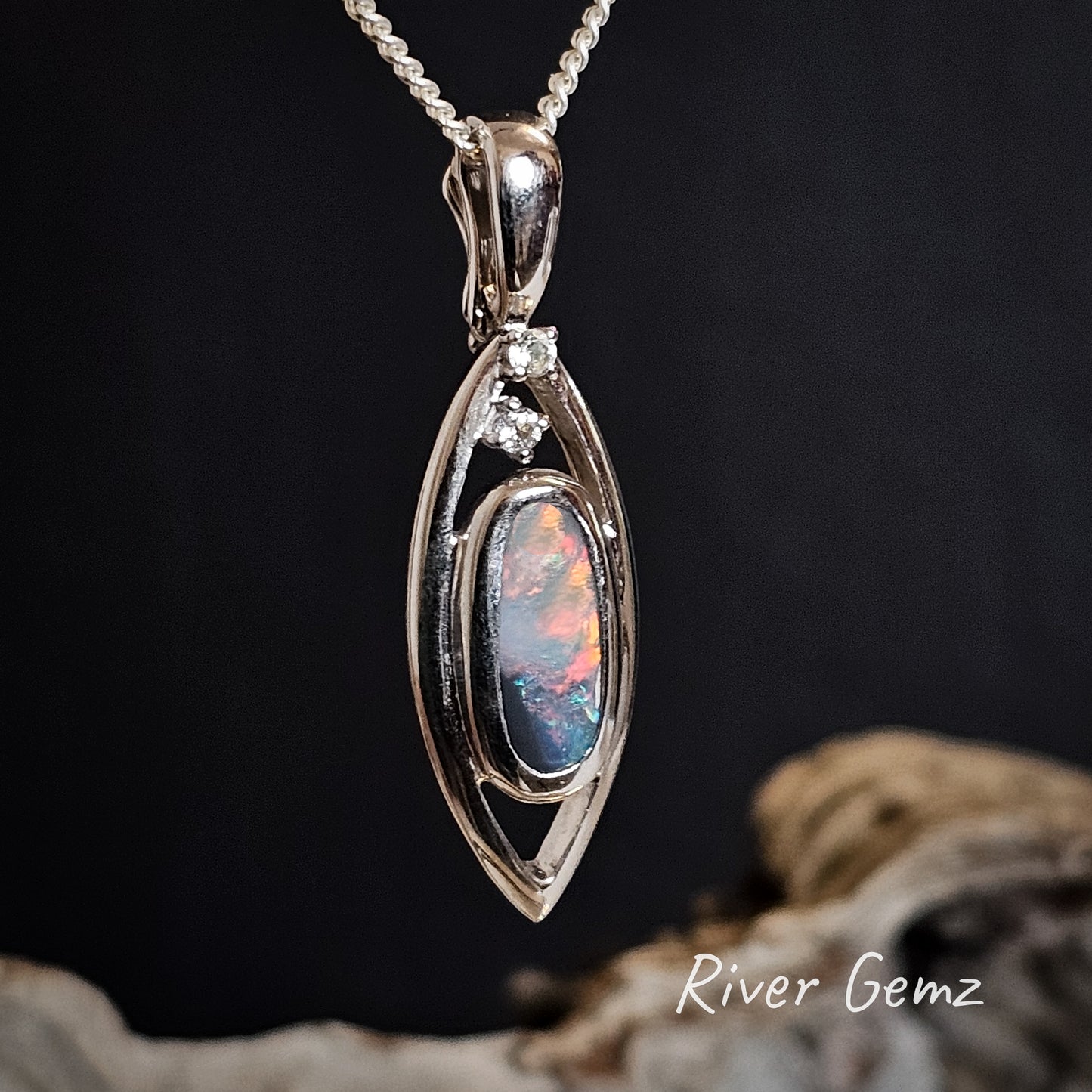 Fire red amongst many other colours visible in the black opal besel set in oblong shaped sterling silver necklace.