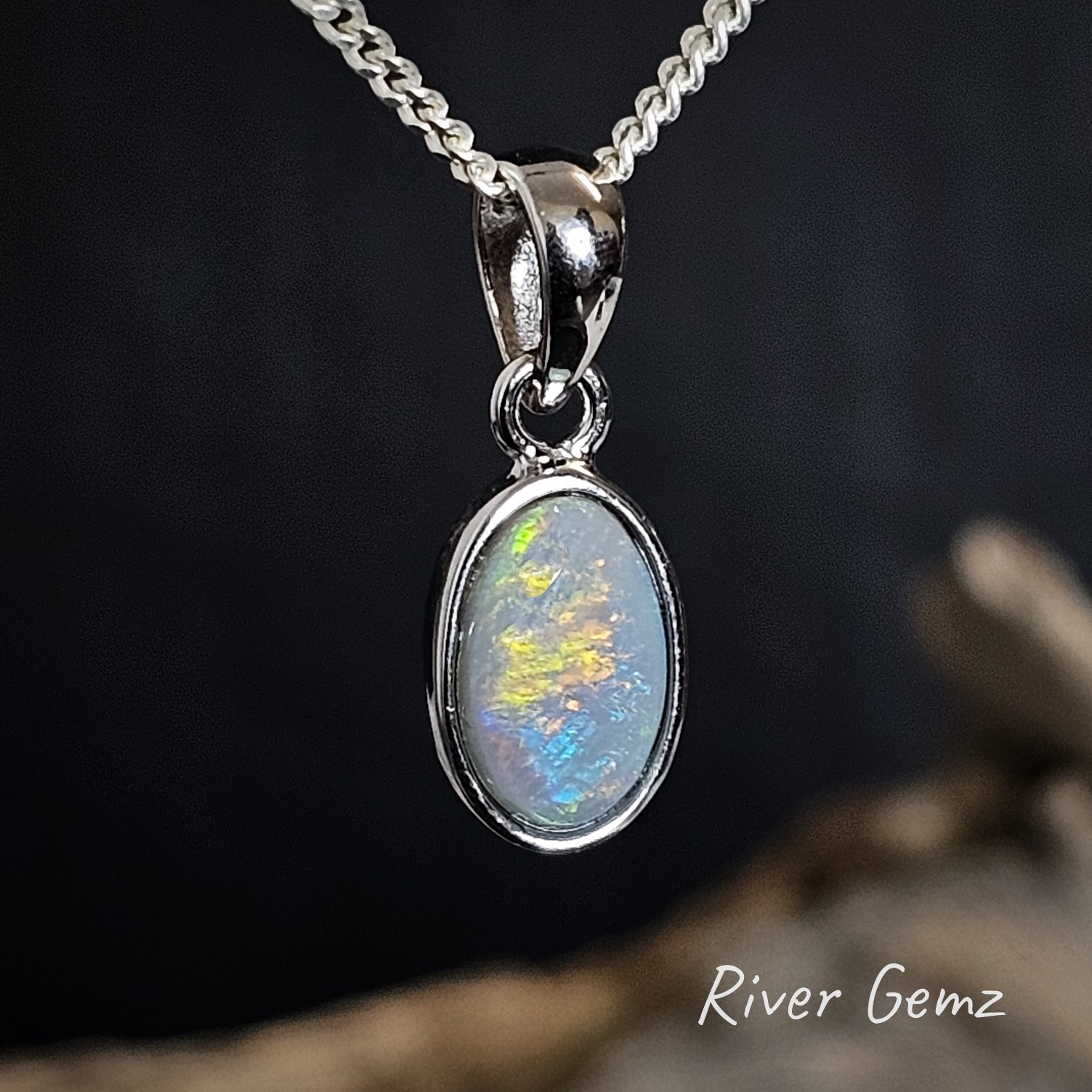 Oval shaped multi-coloured opal pendant necklace on a dark background with 'River Gemz' branding.