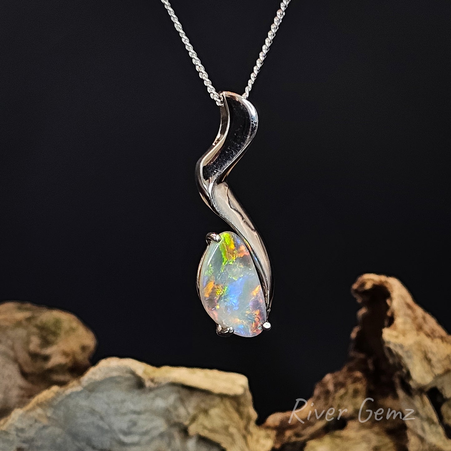 Multi-coloured opal set in silver pendant on a silver chain with a dark background