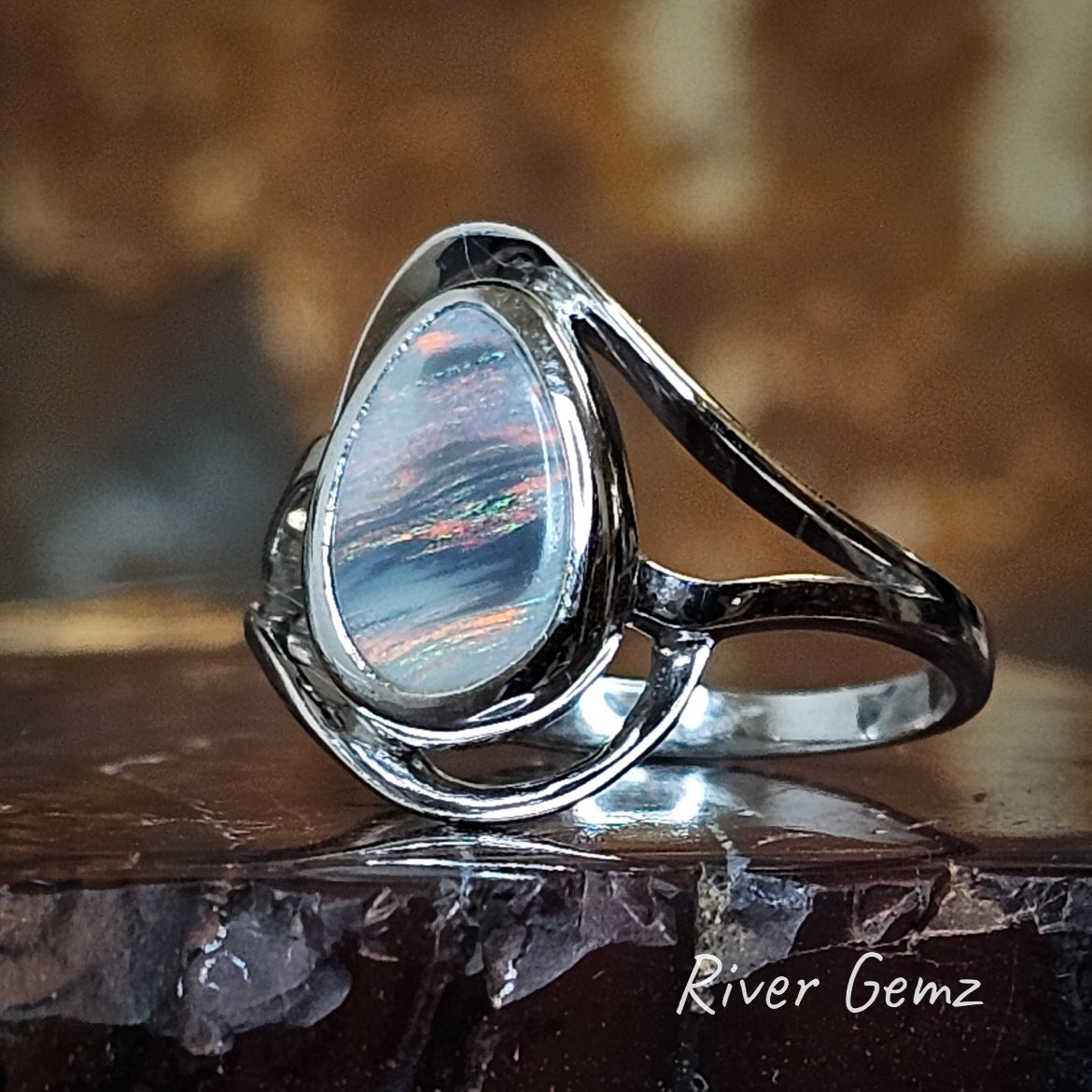 Tear drop shaped multi-coloured dark opal set in silver ring.