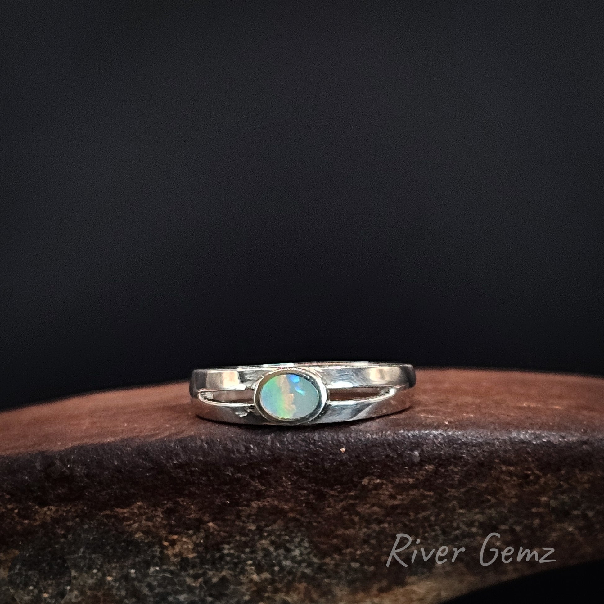 Oval shaped multi-coloured dark opal set in silver ring with split shoulders.