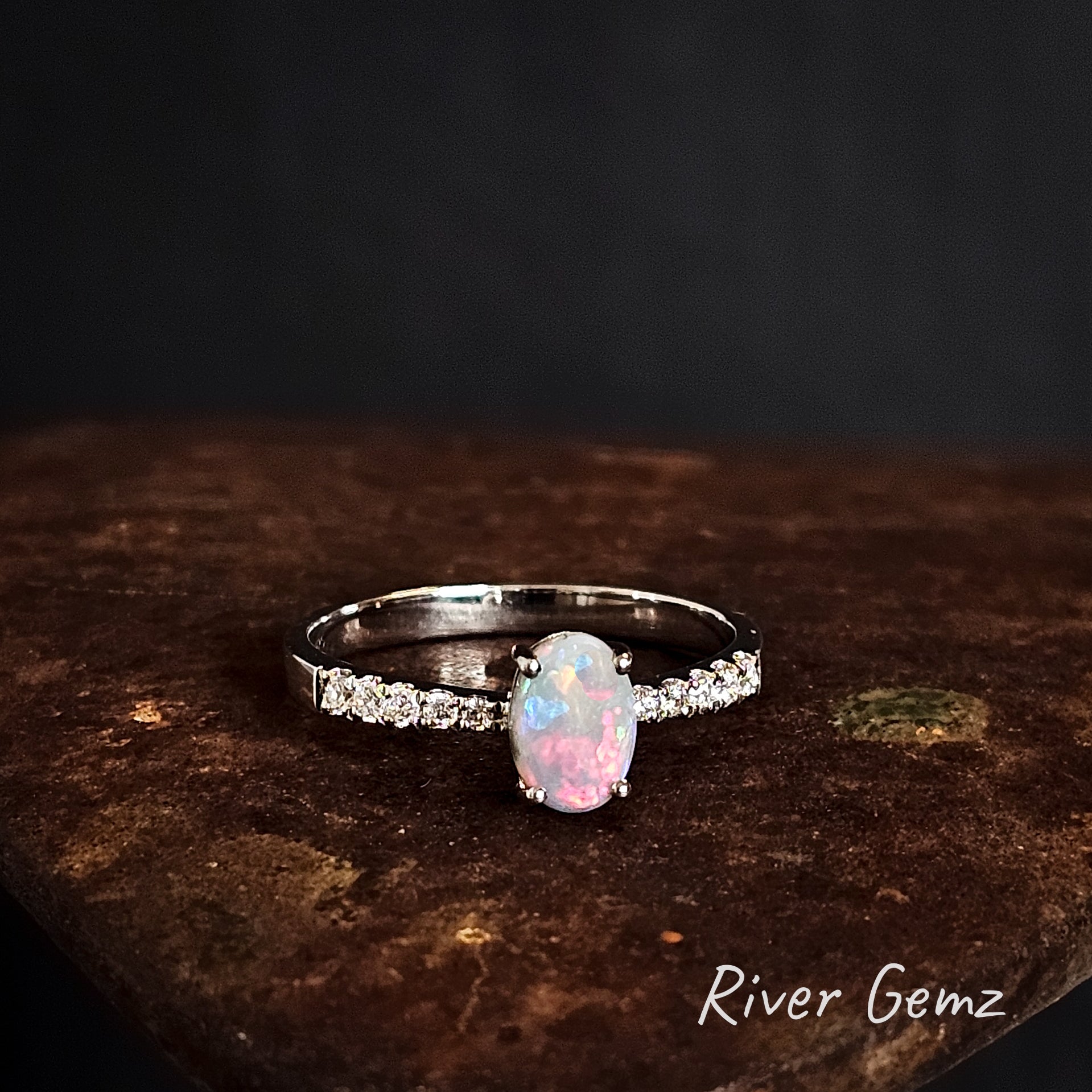 Silver ring with a pink and light green opal and topaz stones on a dark surface, branded 'River Gemz'.