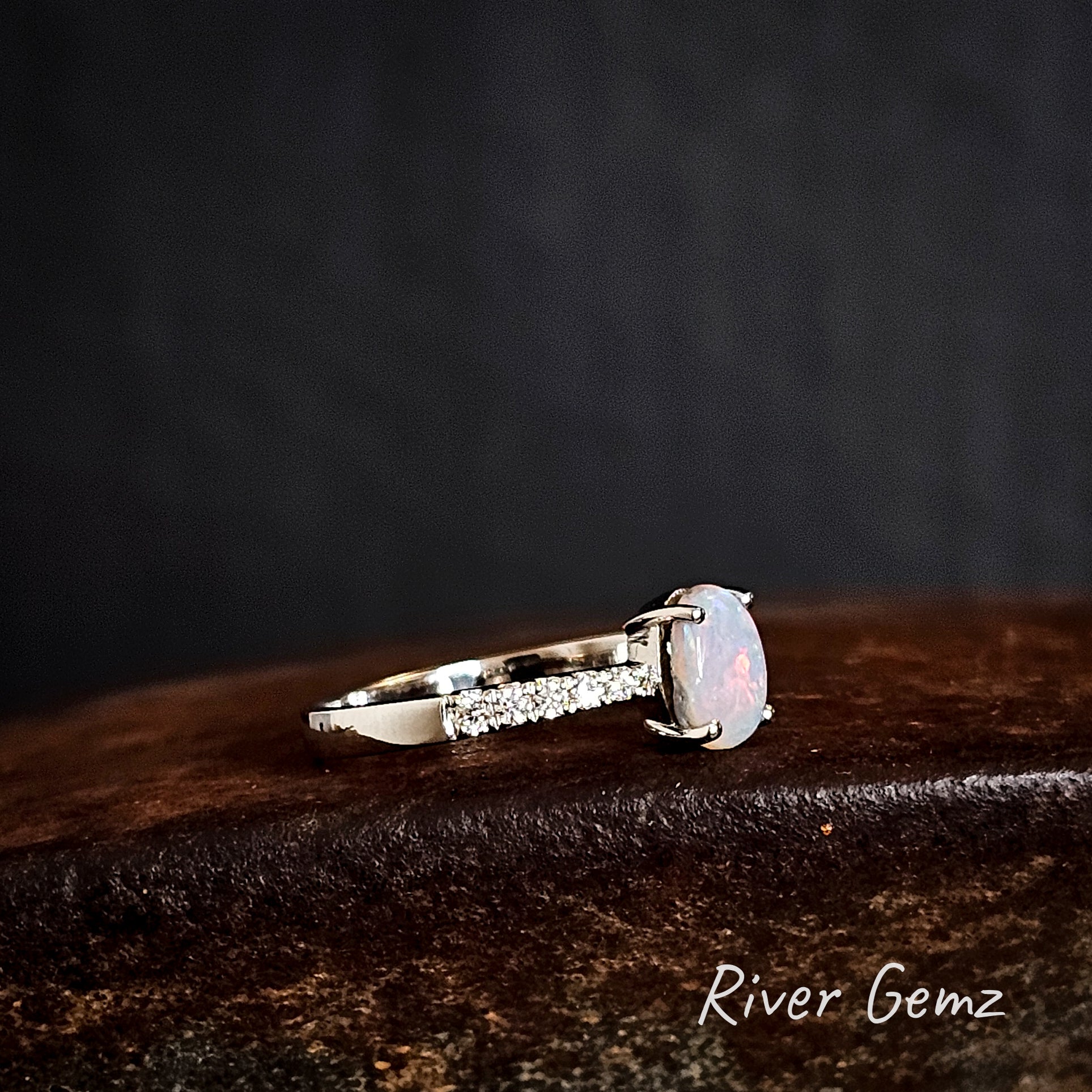 Side view of the ring with a central white opal and topaz stones on a dark surface, branded 'River Gemz'.