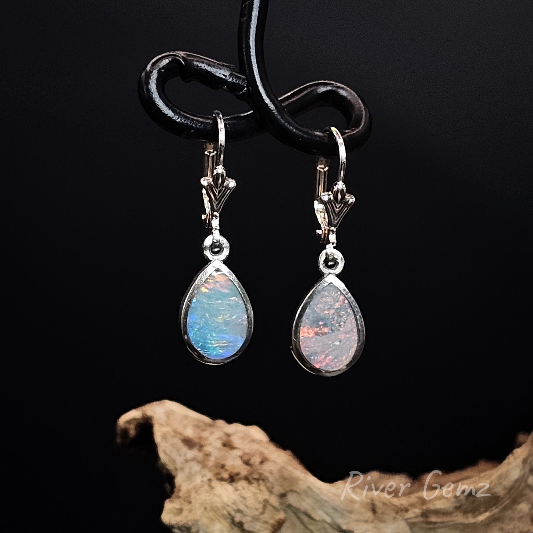 Tear-drop shaped opal earrings on a black stand with a dark background