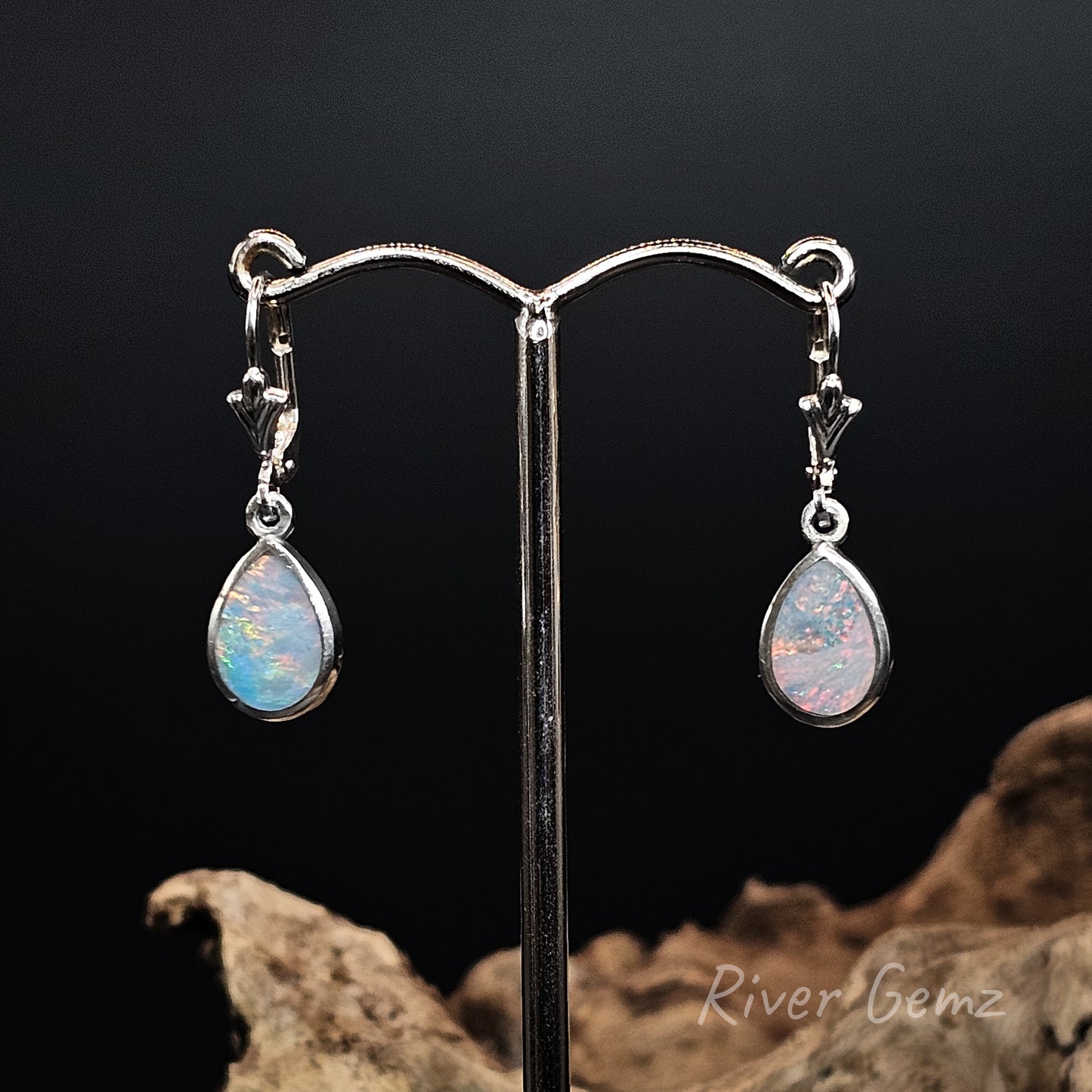 Multi-coloured opal earrings on a stand with a dark background