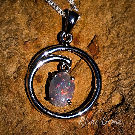 Firy reds amongst this multicoloured black opal claw set in circular sterling silver pendant.