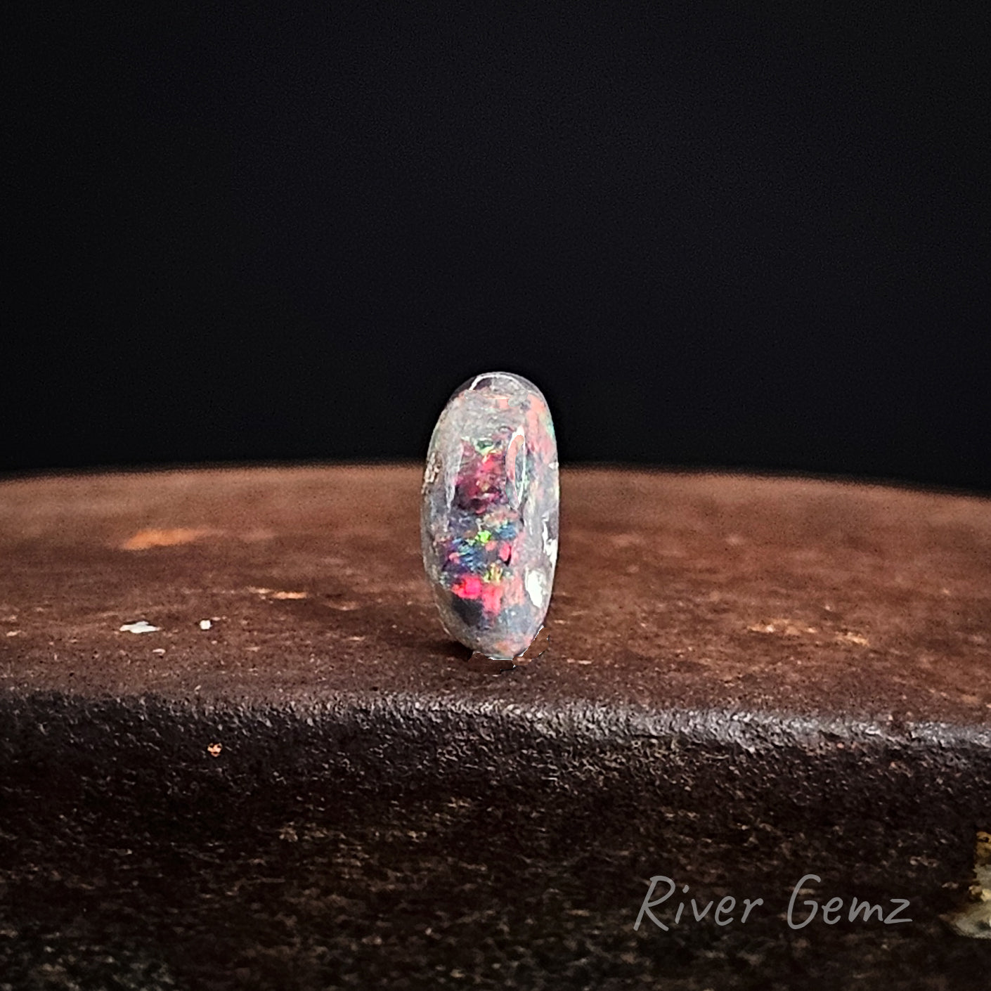 Opal stone on a dark surface with 'River Gemz' branding.