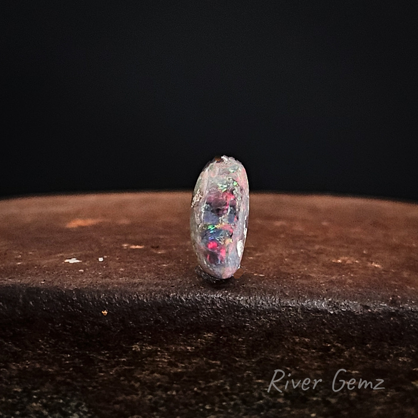 Opal gemstone on a dark surface with 'River Gemz' branding.