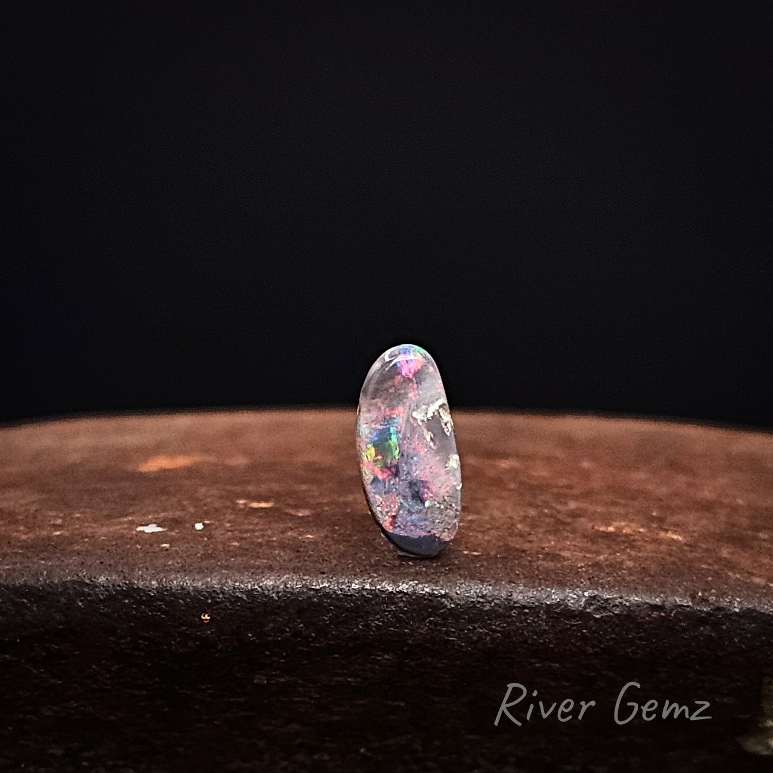 Back of black opal shows unbelievable colour on a dark surface with 'River Gemz' branding.