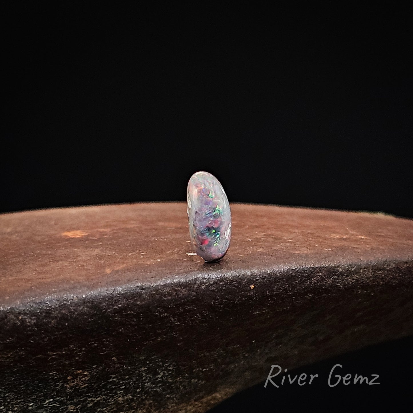 Opal stone on a dark surface with 'River Gemz' branding.