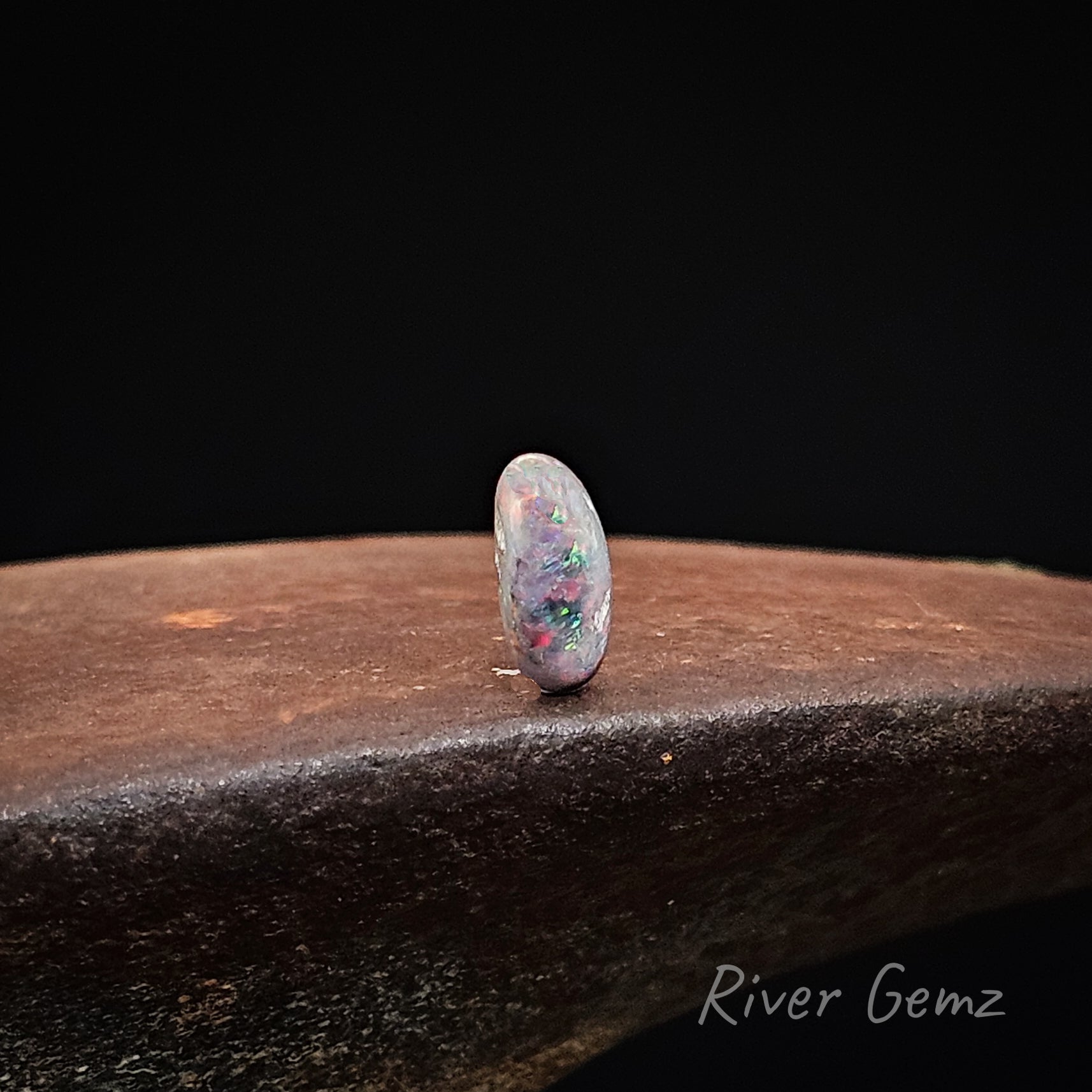 Opal stone on a dark surface with 'River Gemz' branding.