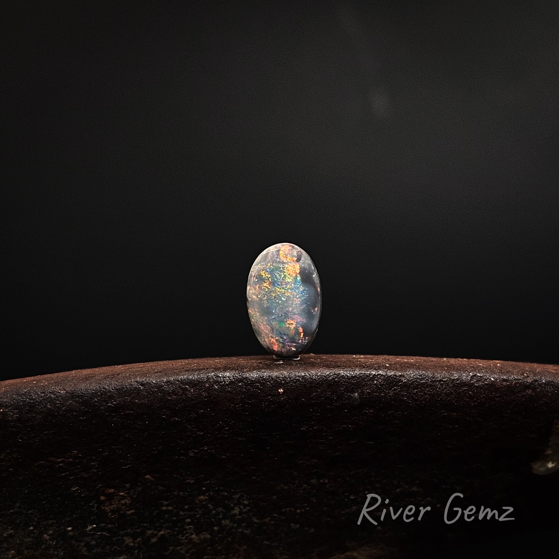 Oval shaped dark opal with all colours standing upright against a black background.