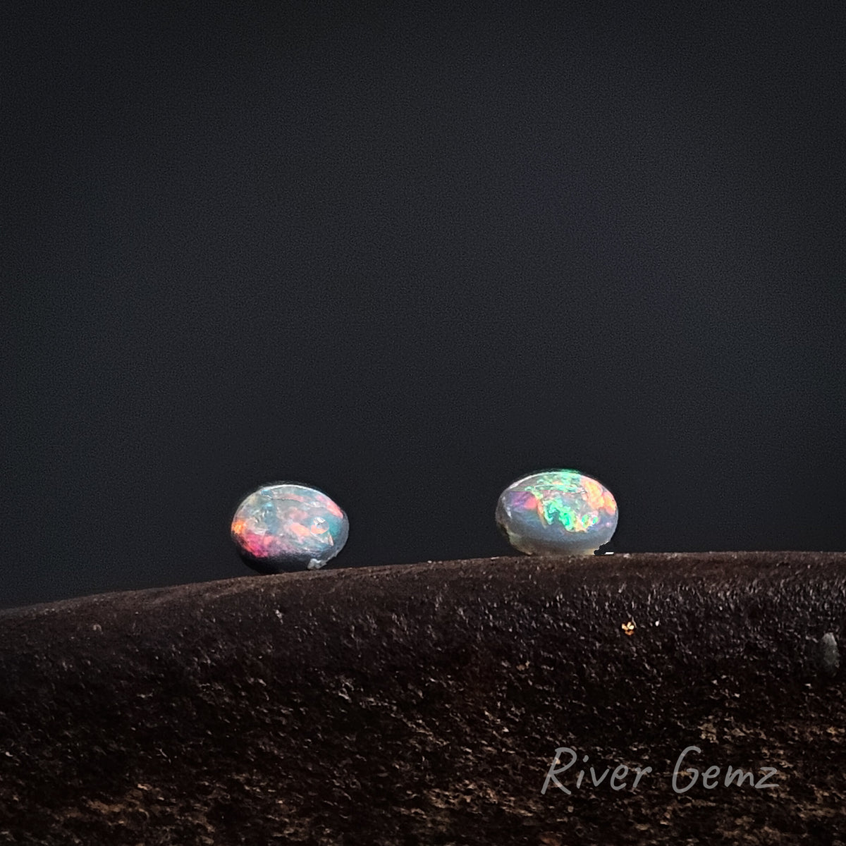 Oval shaped brightly coloured black opals shown in an East-West orientation against a dark background.