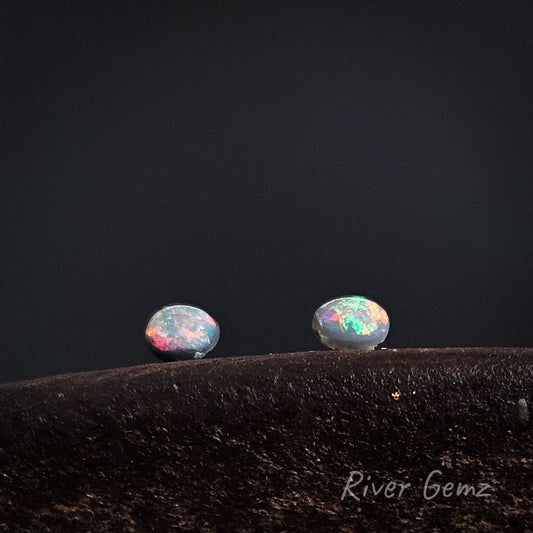 Oval shaped brightly coloured black opals shown in an East-West orientation against a dark background.