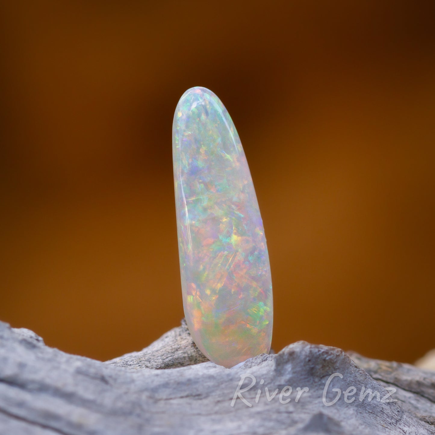 So many flecks of colour and variations of colour in this opal are shown. The opal sits upright on a piece of light-grey driftwood in each of the images.