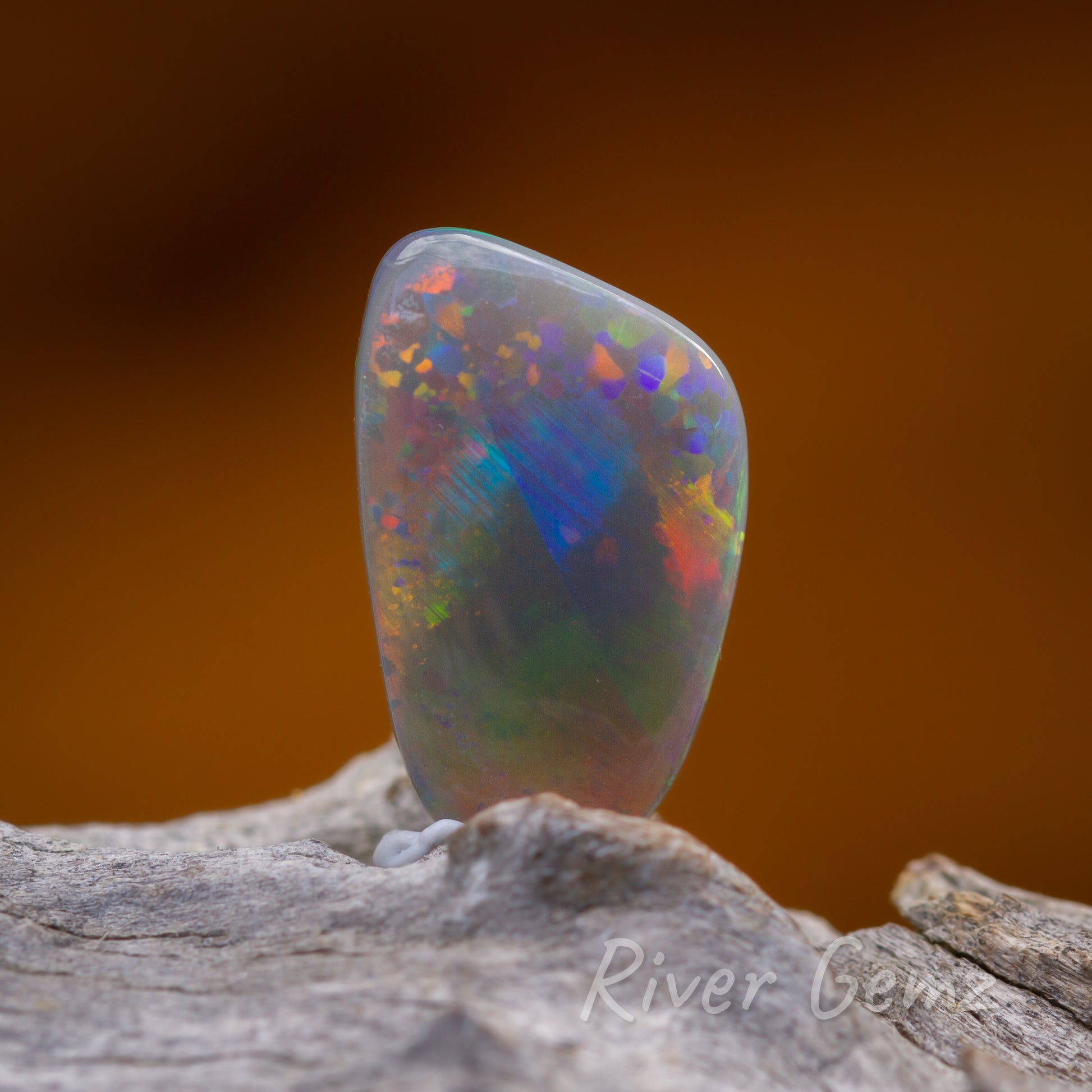 Front view of multicoloured dark opal sitting upright on a light grey wood.