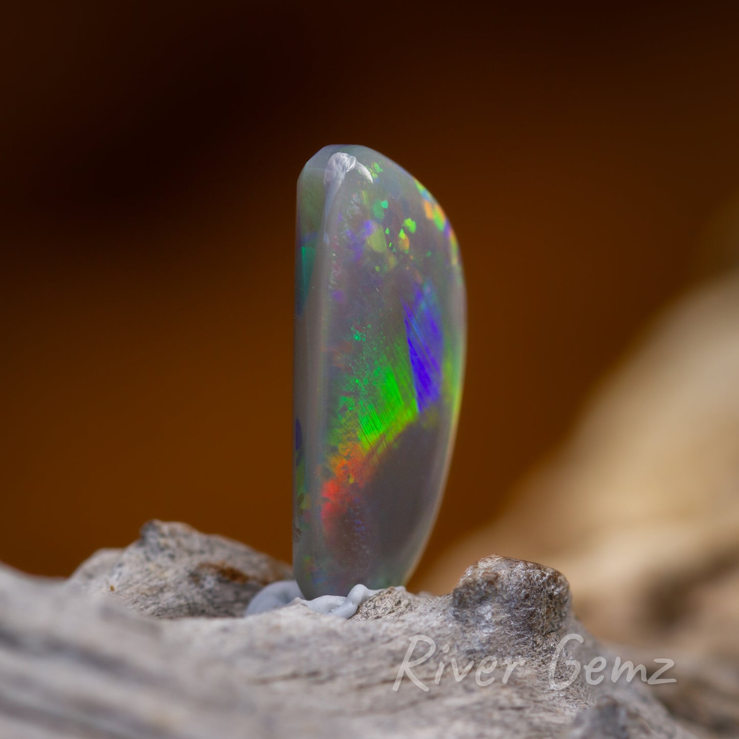 Side view of multicoloured dark opal sitting upright on a light grey wood.