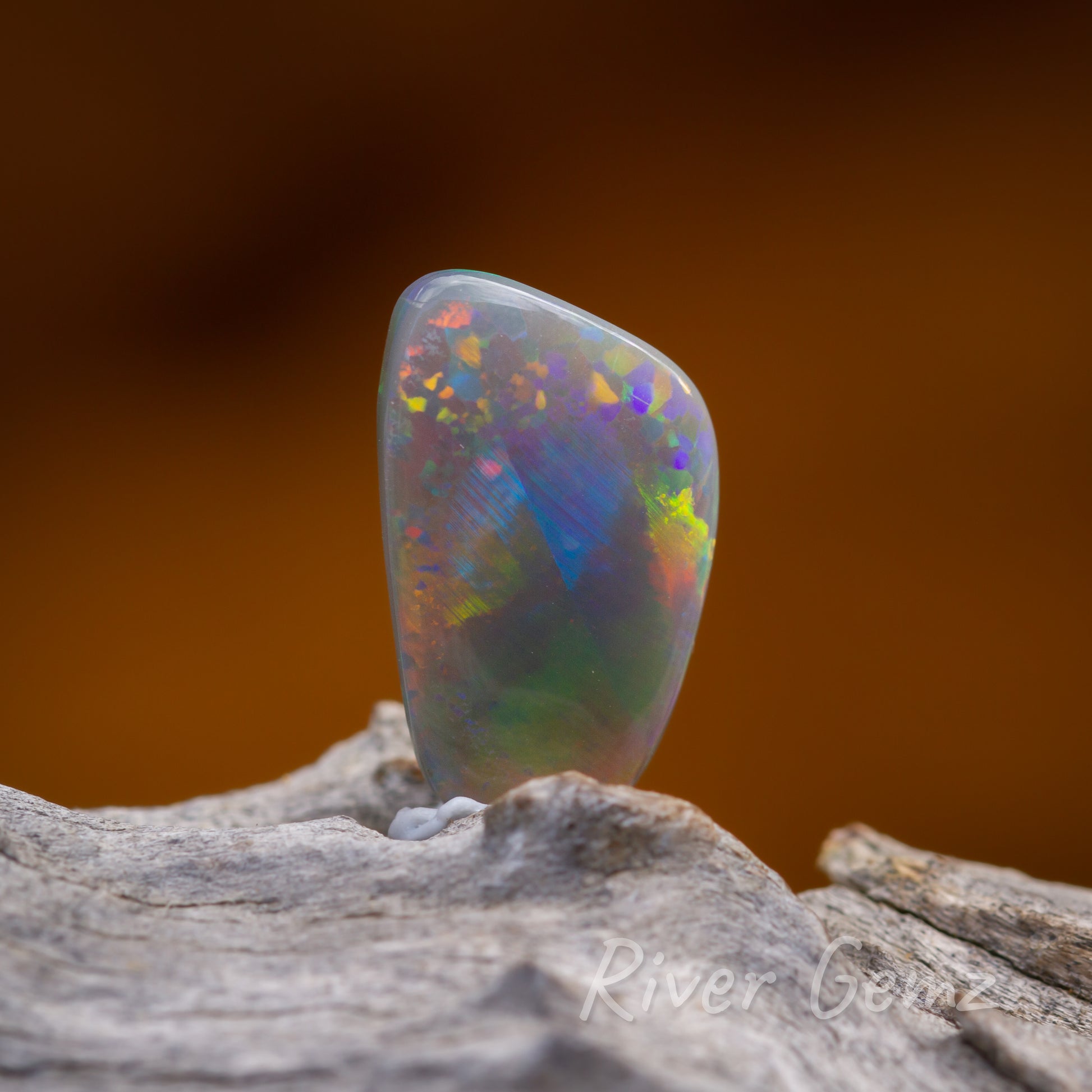 Second front view of multicoloured dark opal sitting upright on a light grey wood.