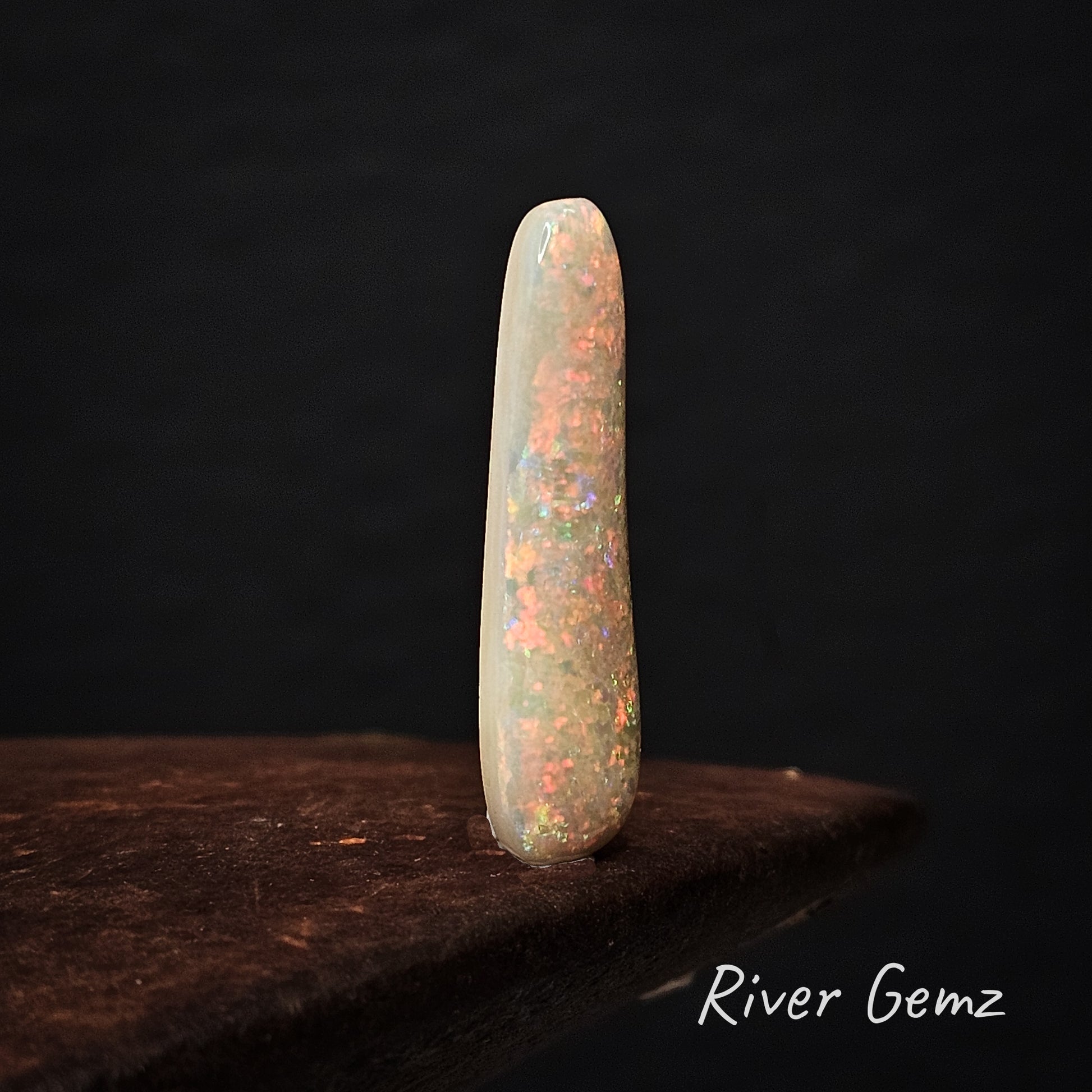 Colourful white opal standing upright on a dark surface with 'River Gemz' branding.