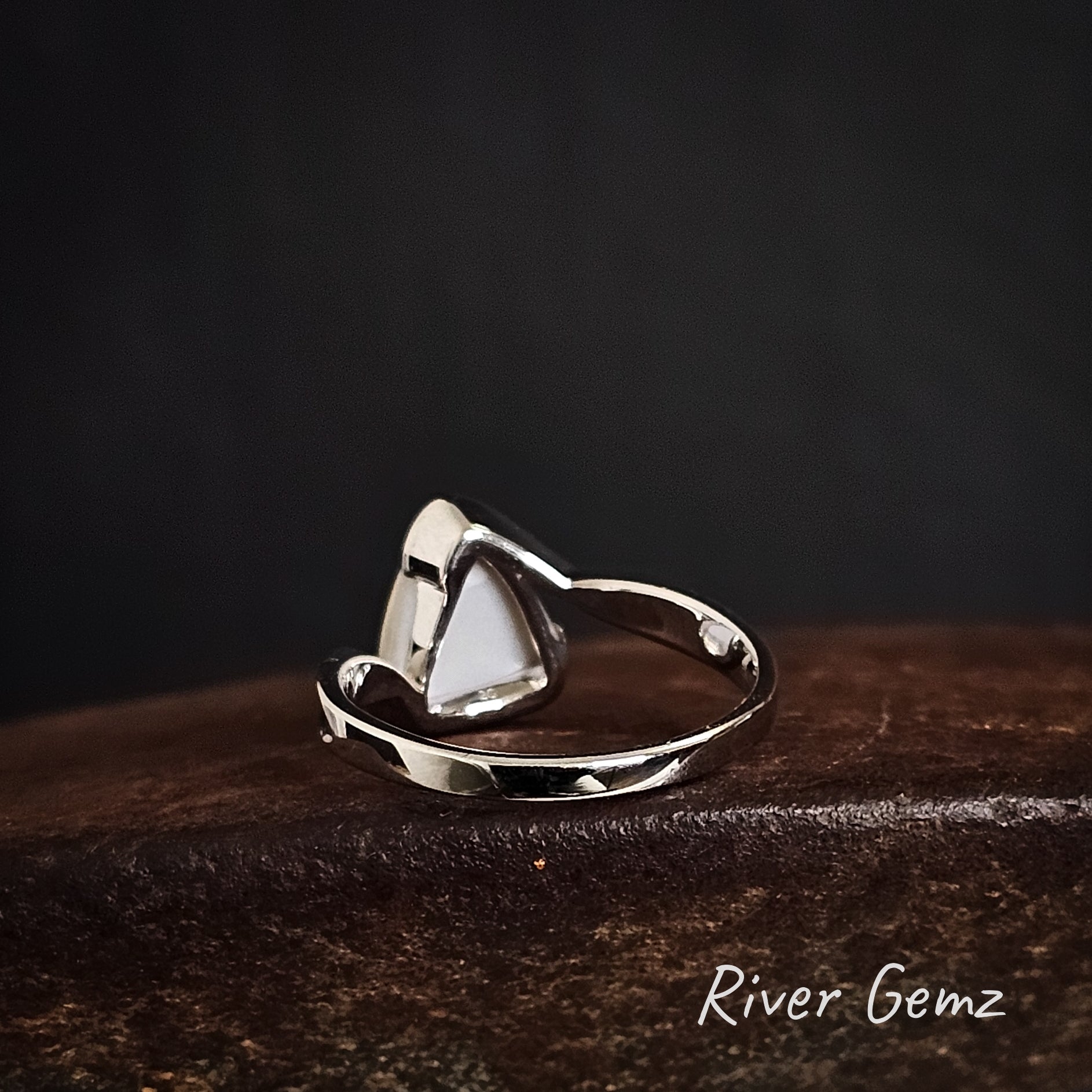 Back of silver ring showing the light tone base of the white opal on a dark surface, branded 'River Gemz'.