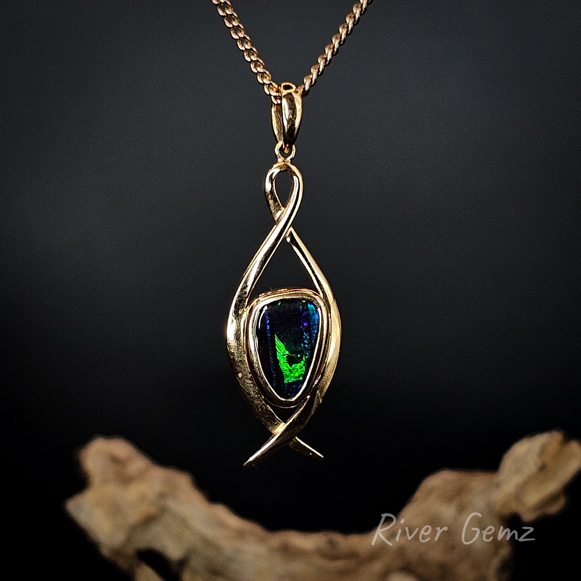 Gold pendant with green gemstone on a dark background, featuring 'River Gemz' branding.