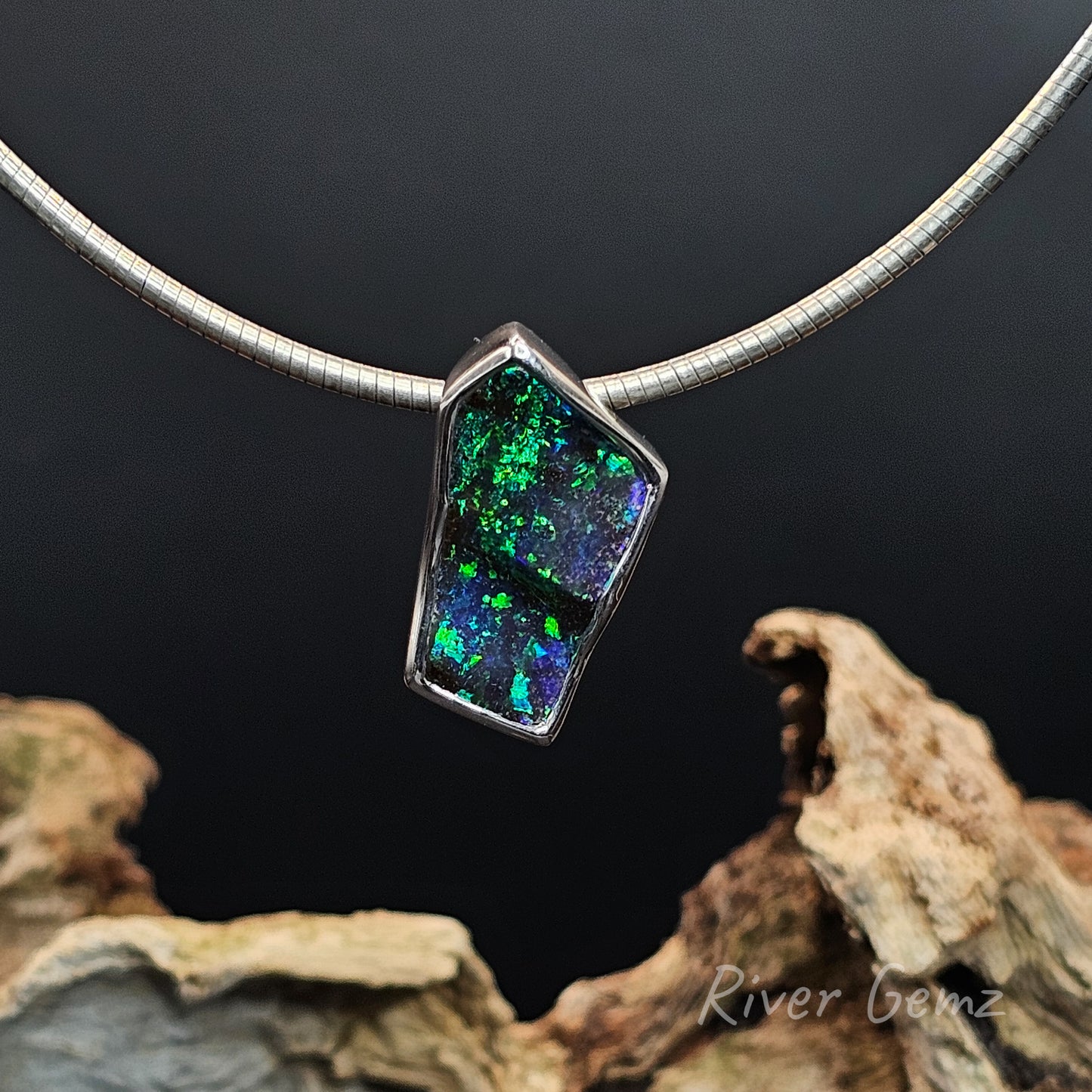 Necklace with a pendant featuring green and blue black boulder opal on a dark background.