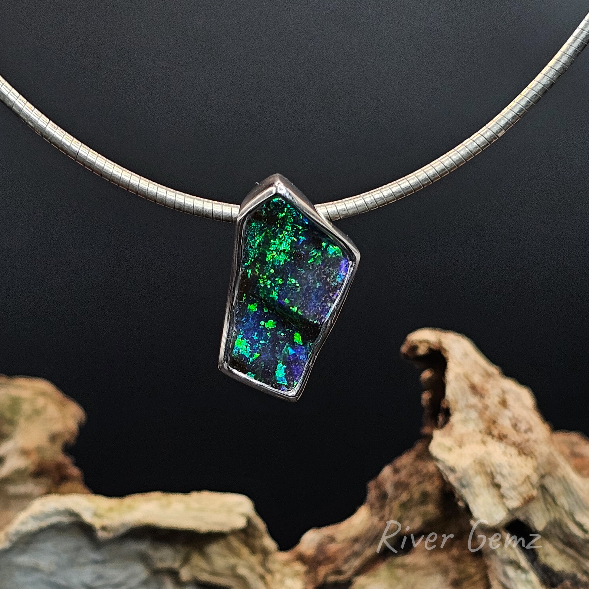 Necklace with a pendant featuring green and blue black boulder opal on a dark background.