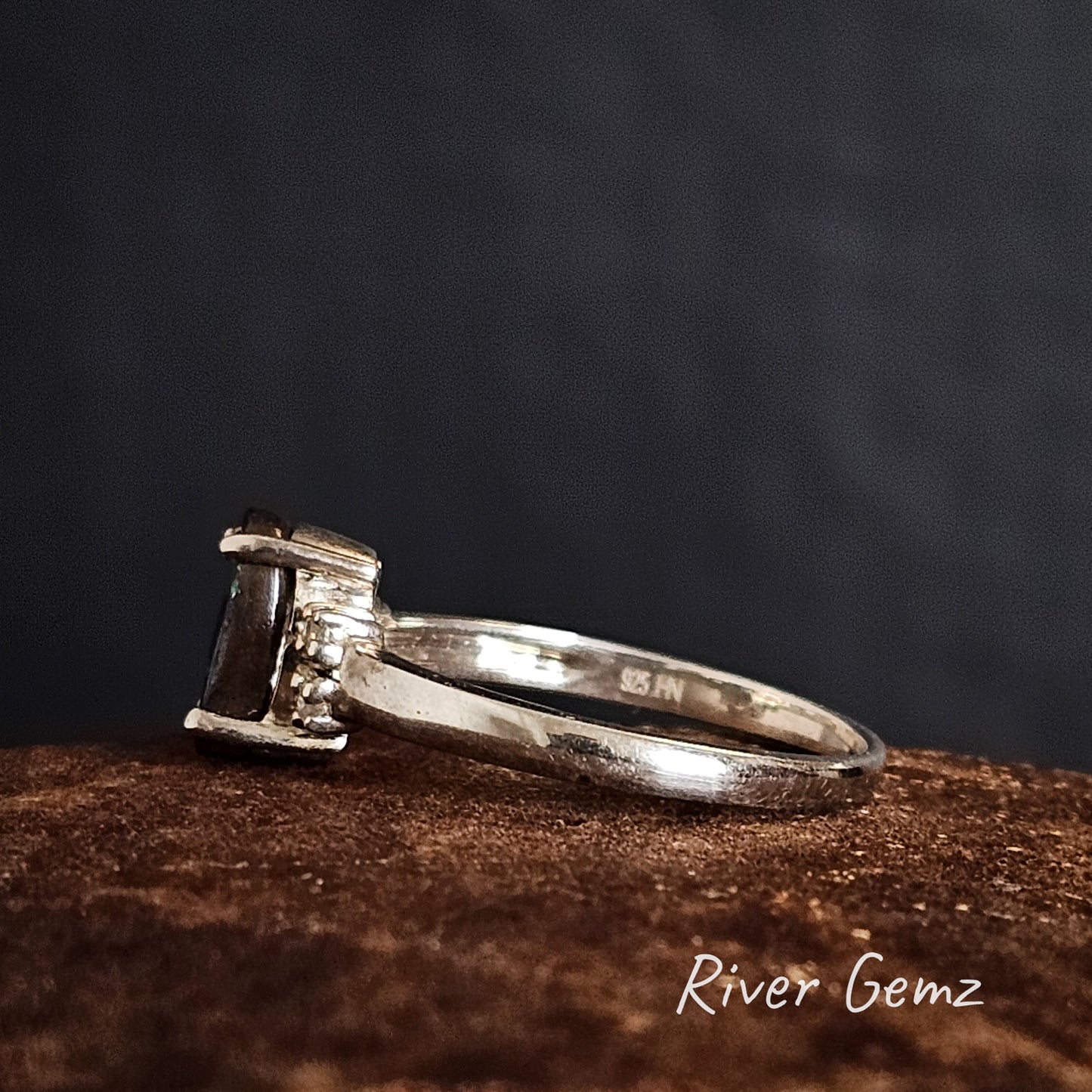 Side view of the ring showing the 925 stamp for sterling silver with a gemstone on a dark background, branded 'River Gemz'.