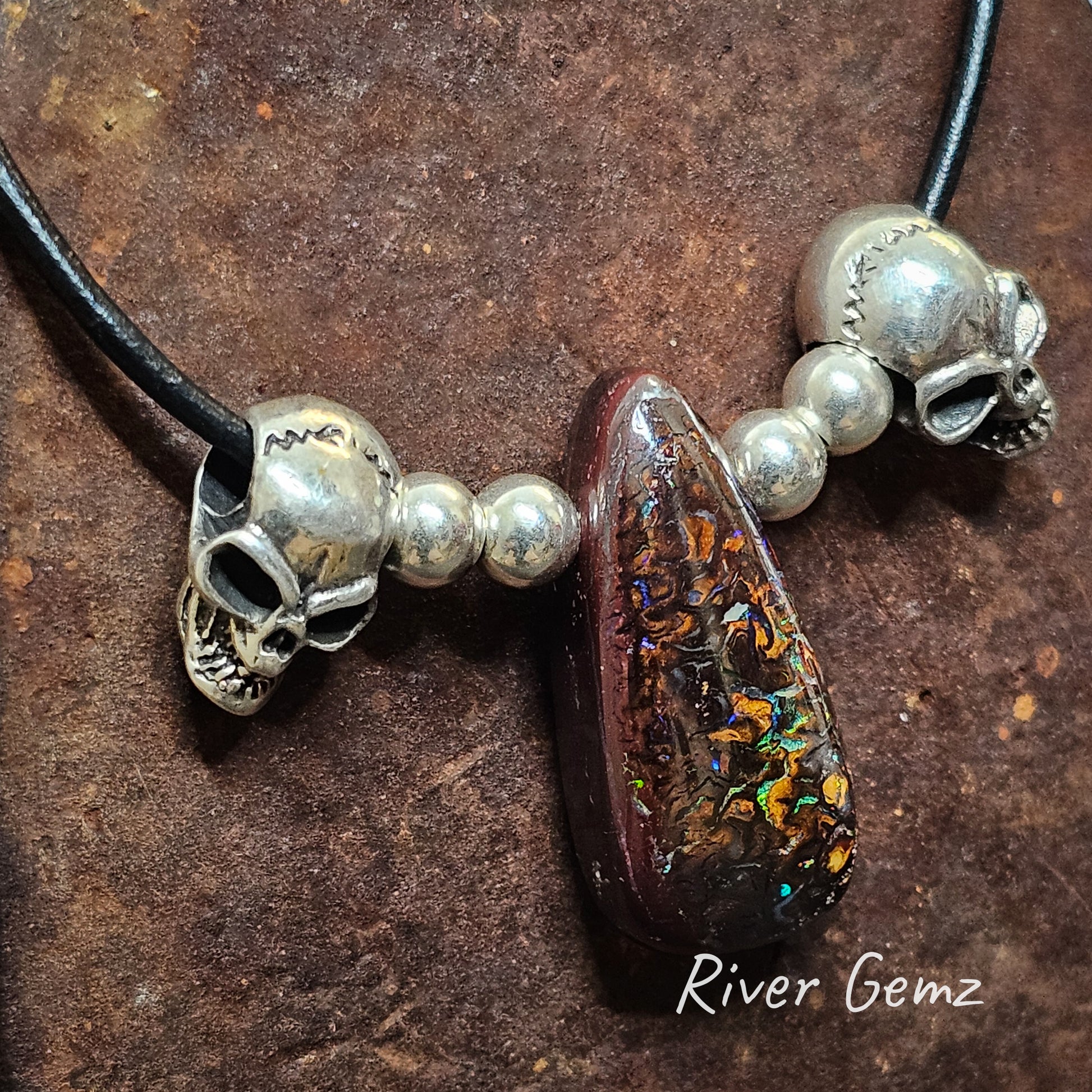 Dark brown opal with squiggles of colour with 2 silver beads and a skull on each side all strung on black leather necklace.