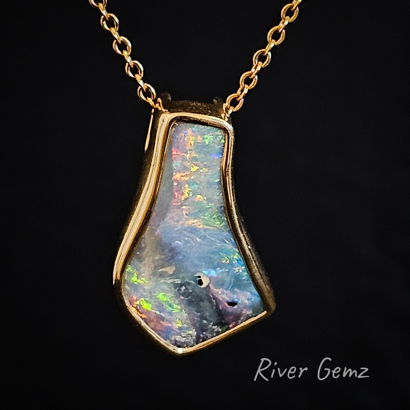 Freeform cut multi-coloured boulder opal set in gold pendant.