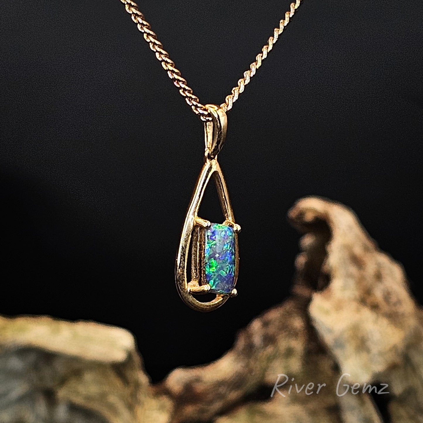 Gold pendant with a colourful gemstone on a dark background, featuring 'River Gemz' branding.