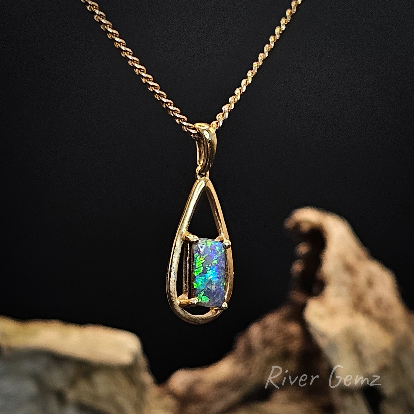 Gold pendant with a colorful gemstone on a dark background, featuring 'River Gemz' branding.