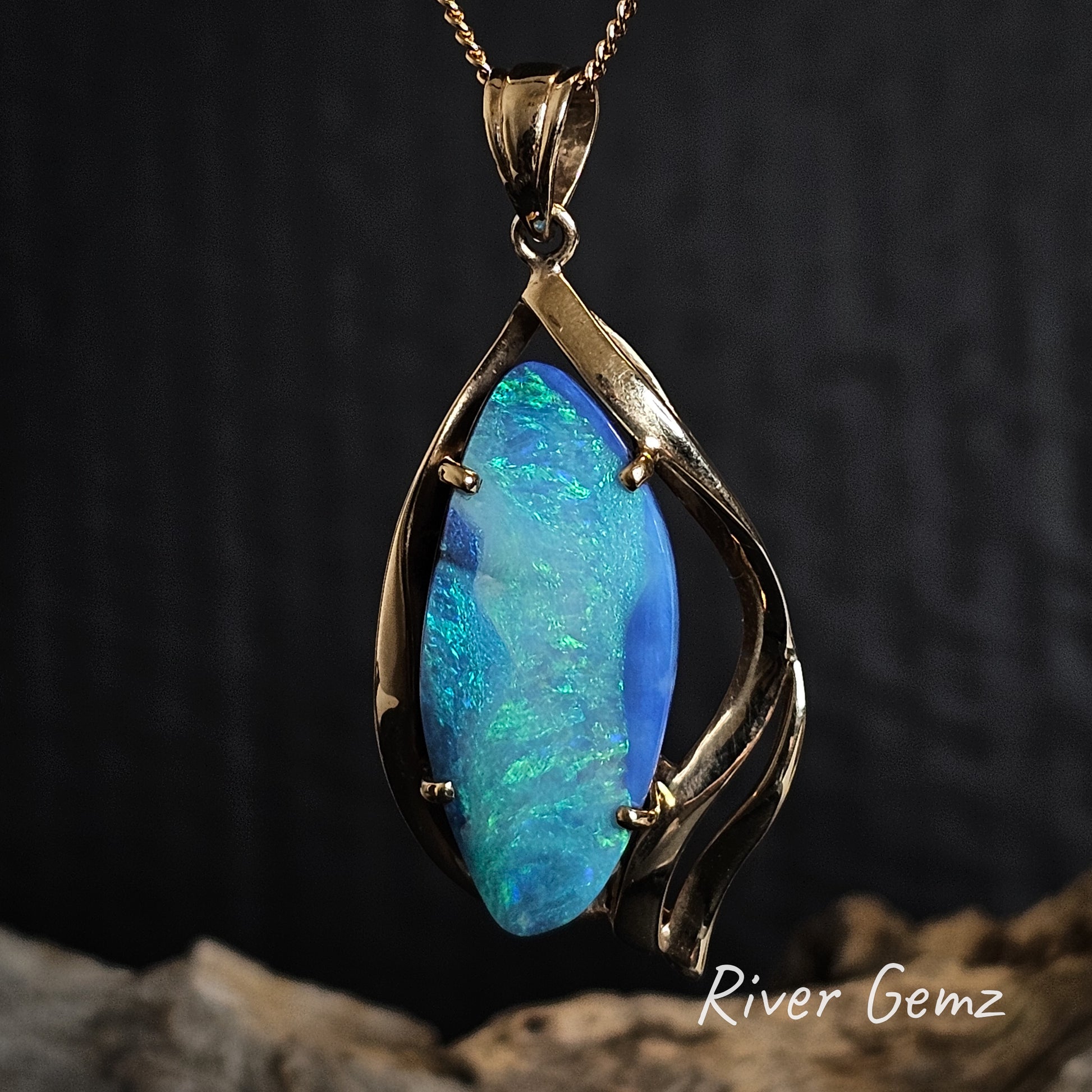Large blue and green boulder opal claw set in yellow gold necklace on a dark background, branded 'River Gemz'.