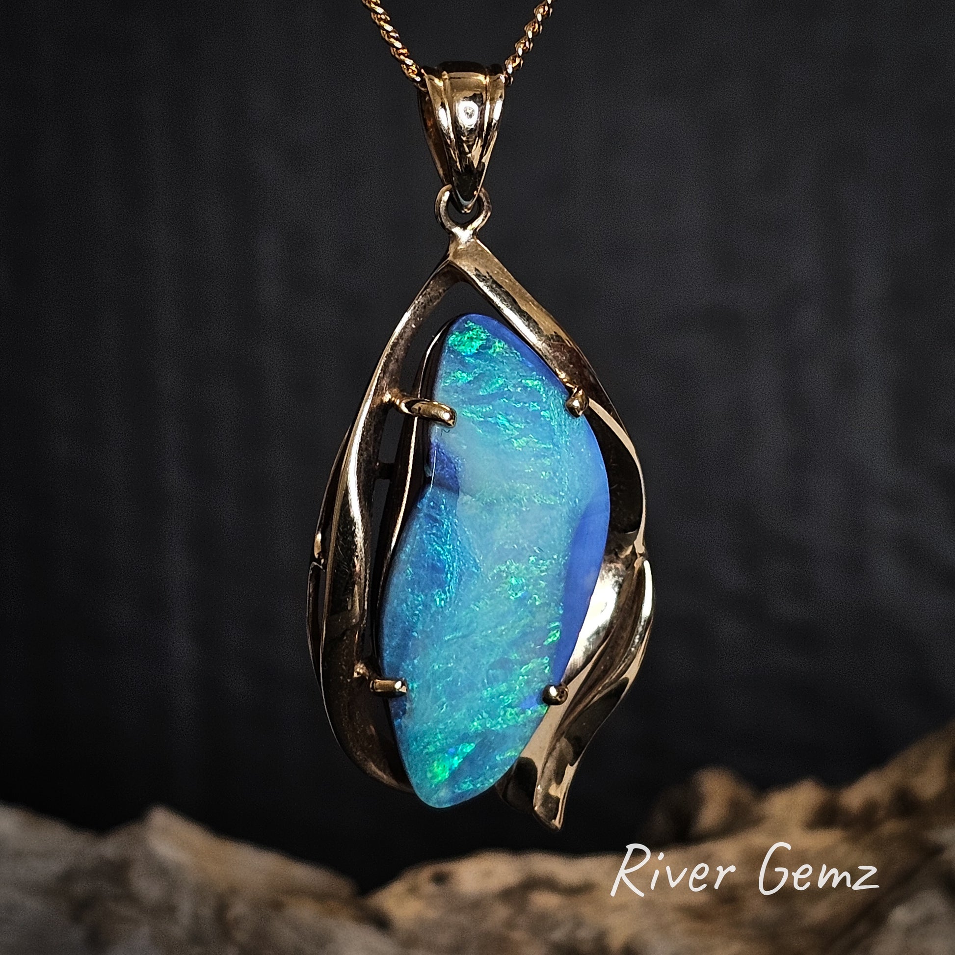 Opal pendant with gold setting on a dark background, featuring the brand 'River Gemz'.