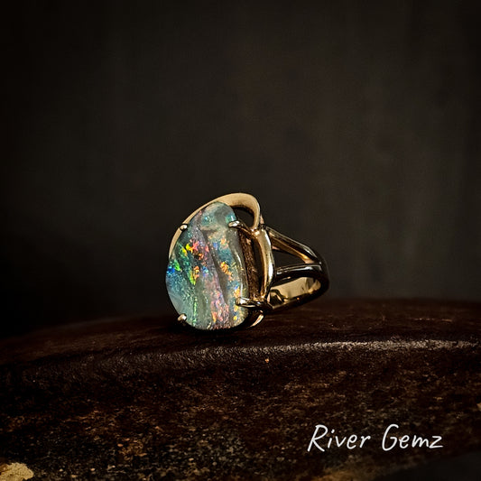 Yellow gold ring with a large colorful boulder opal on a dark background, featuring the brand 'River Gemz'.